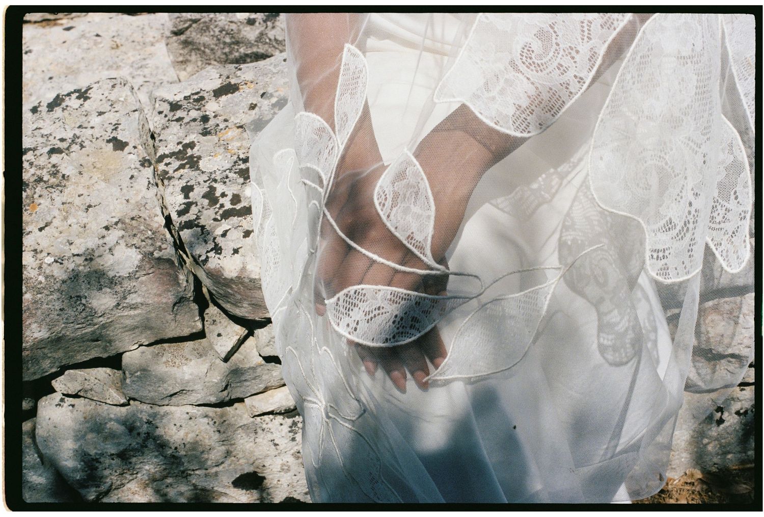 Close-up of a bride wearing lace wedding dress and strappy heels standing on rustic stone ground.