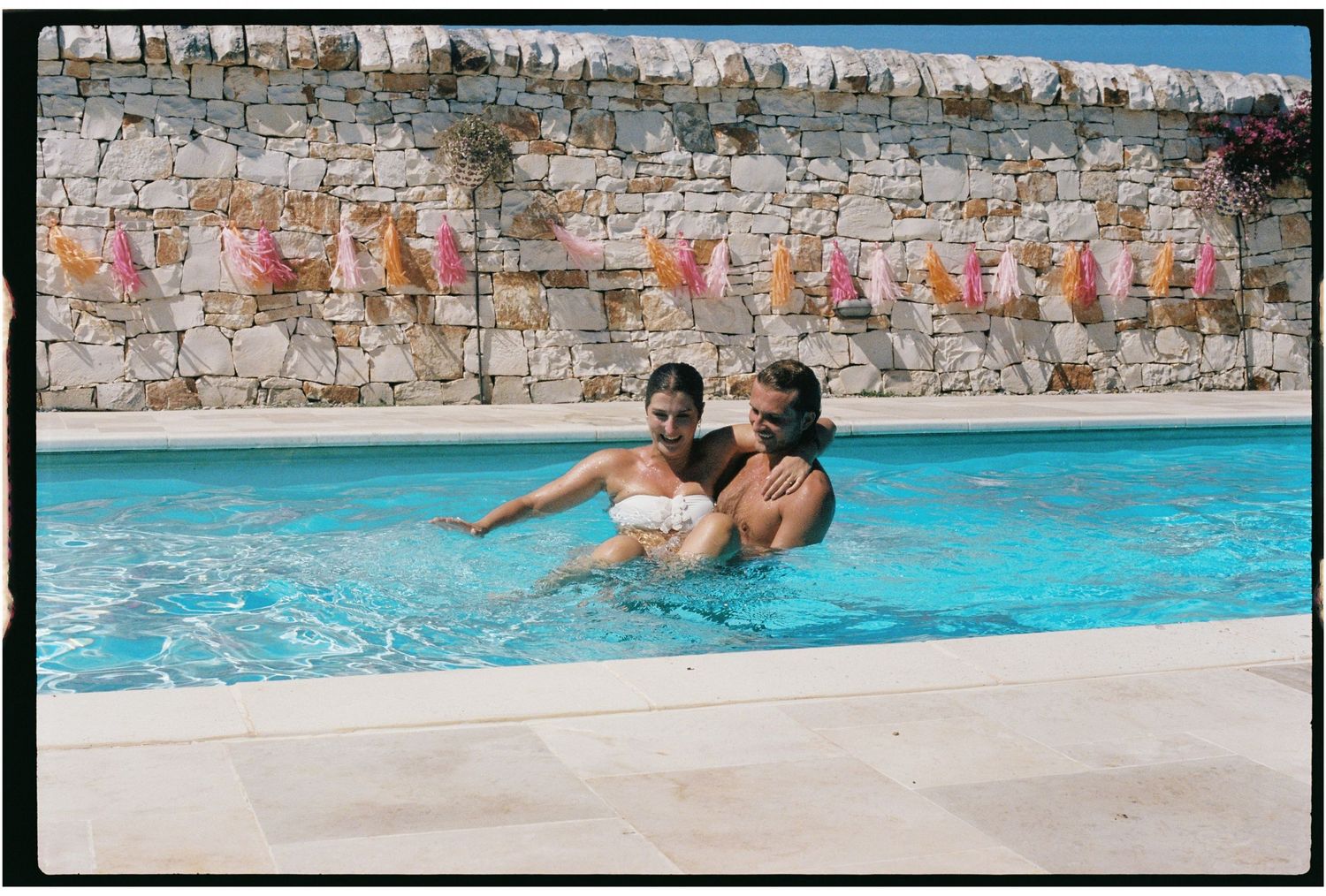 Couple laughing and playing together in a sunny outdoor swimming pool on holiday.
