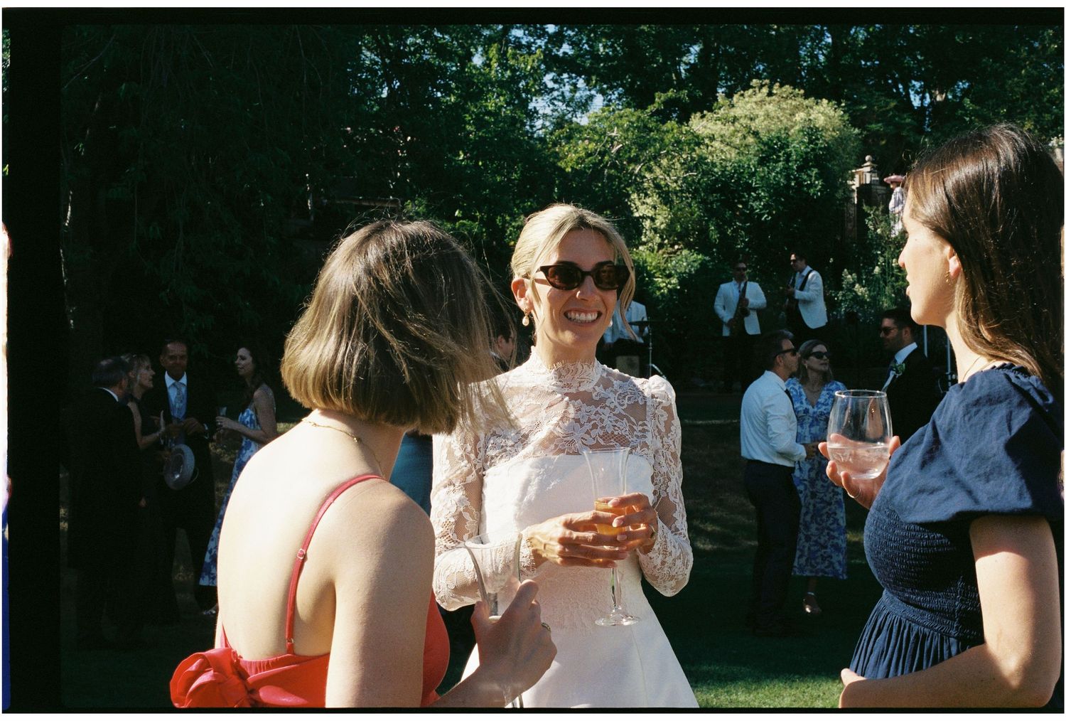 Smiling bride in lace dress socializing with guests at an outdoor garden wedding reception.