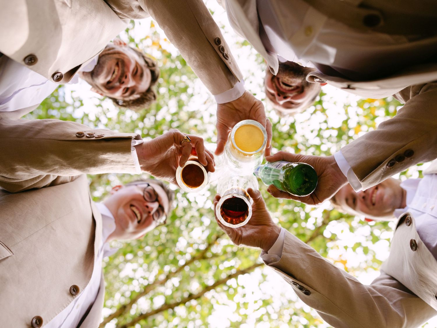 Friends toasting with colorful drinks from above against green foliage background.