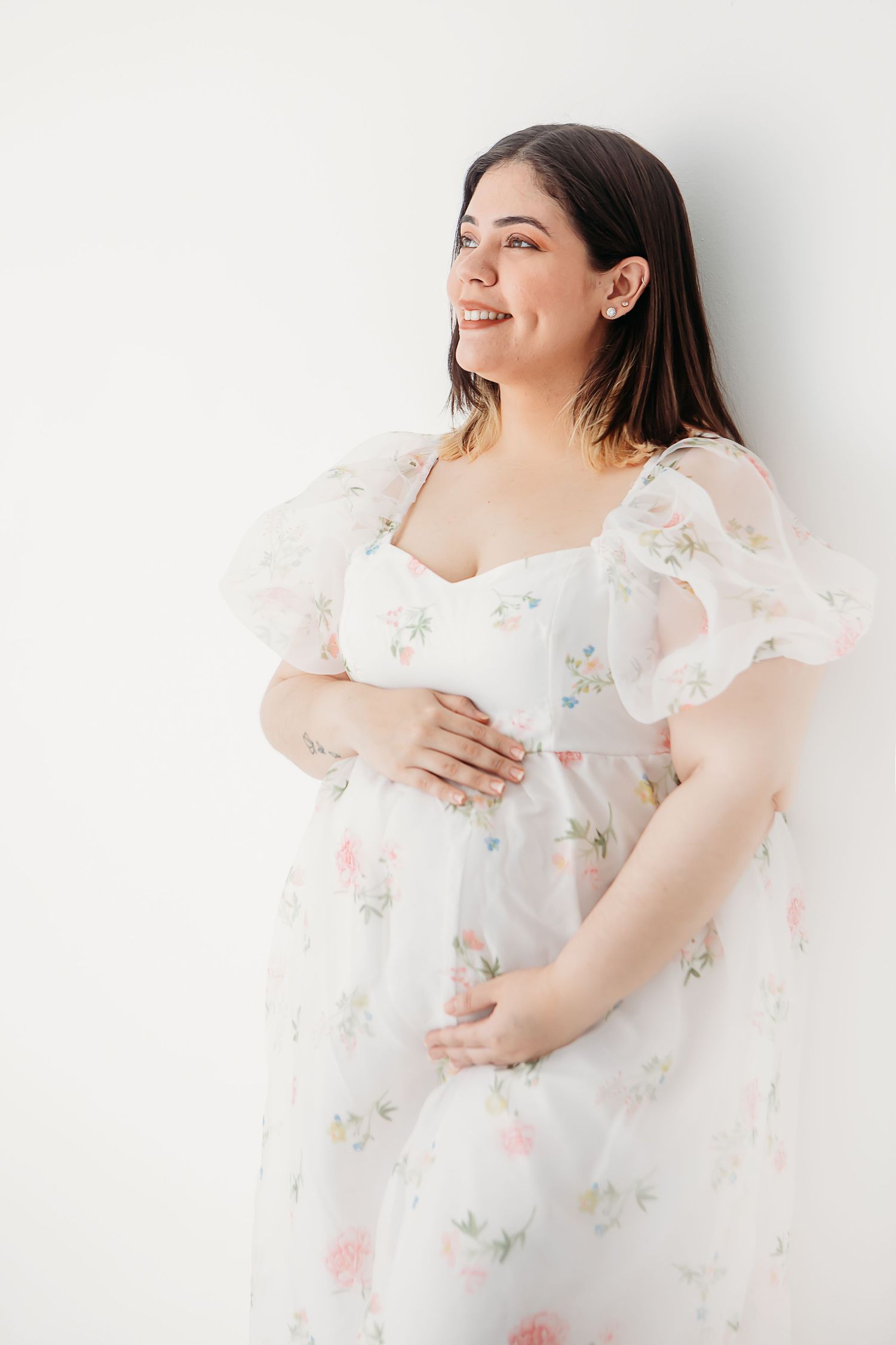 Woman in white floral dress poses against white backdrop in elegant portrait series.