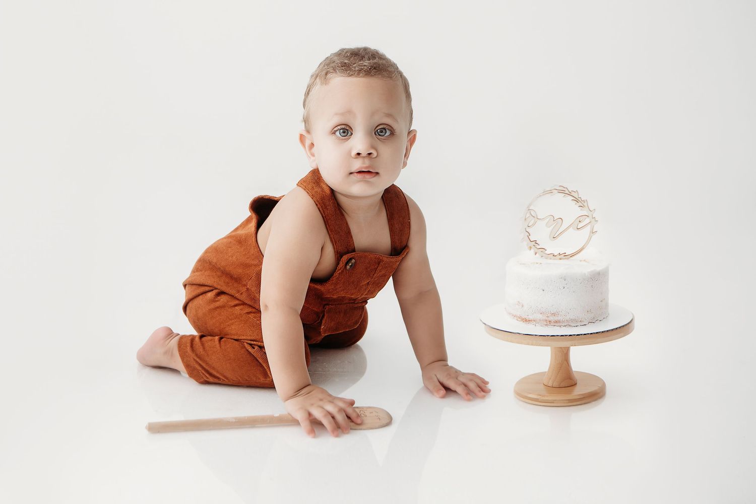 Baby in rust-colored romper crawls during minimalist photo session with wooden props.