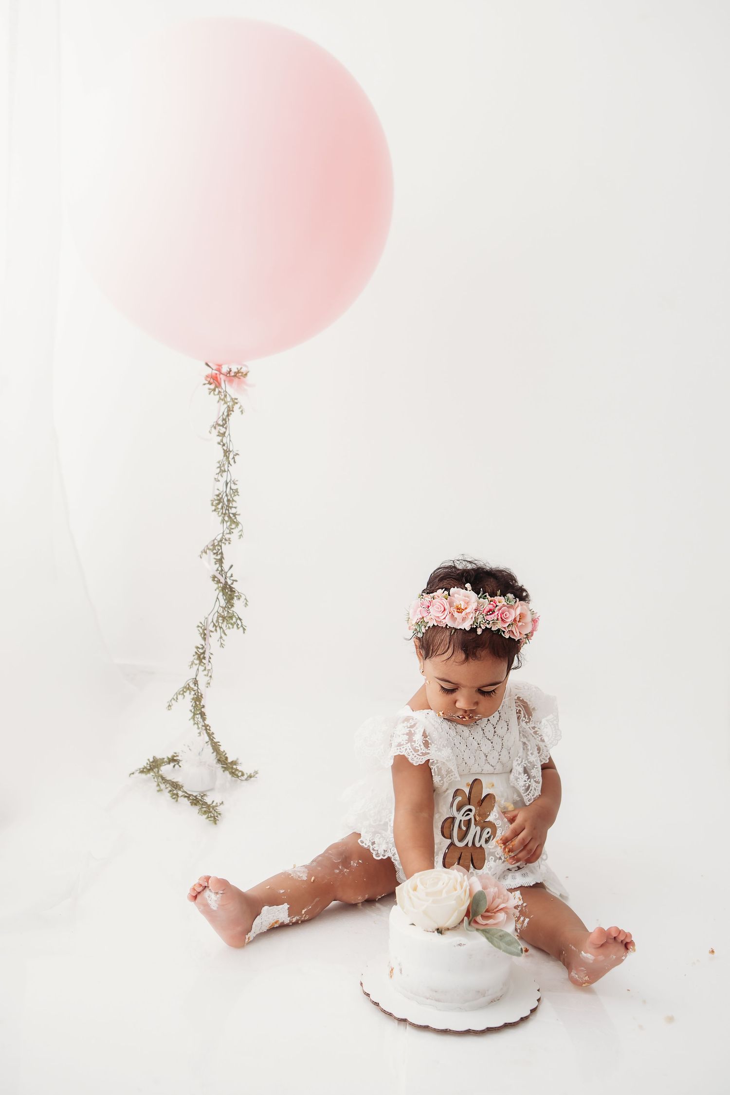 Large pink balloon and white cake against minimalist backdrop with floral accents.