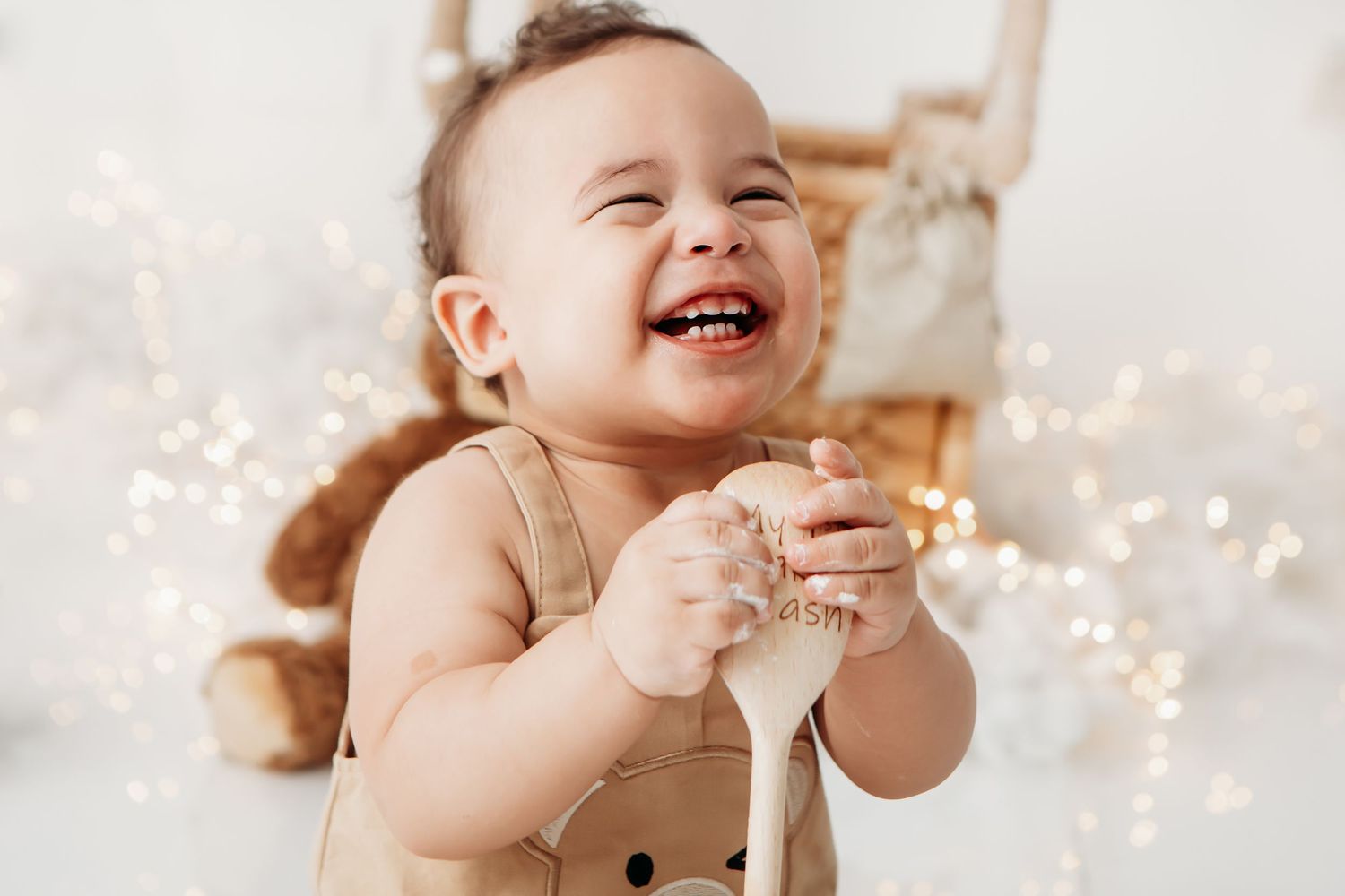 A laughing baby sits in a chair with glowing sparklers and festive bokeh lights in the background.