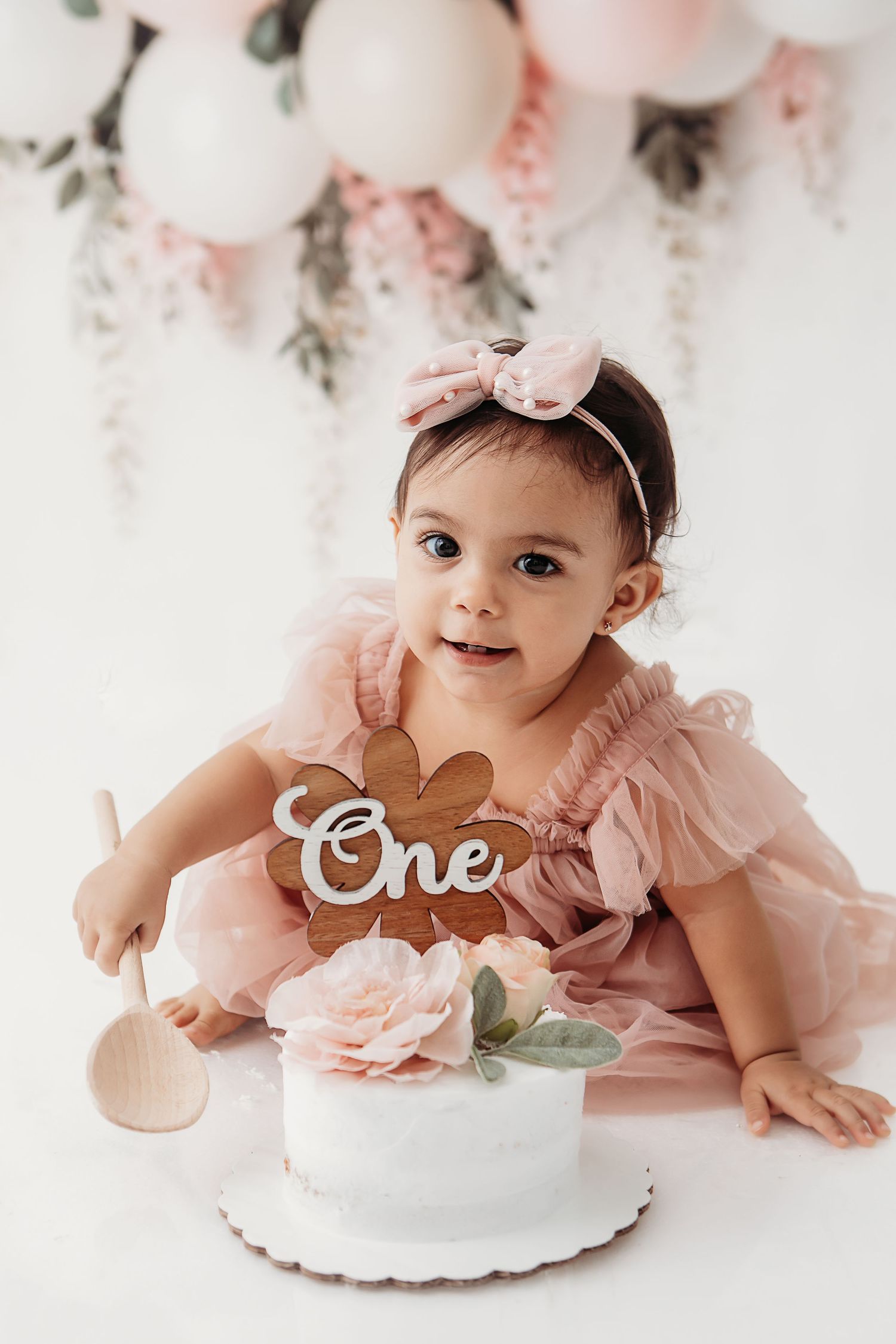Pink floral backdrop with white cake decorated with 'One' text.
