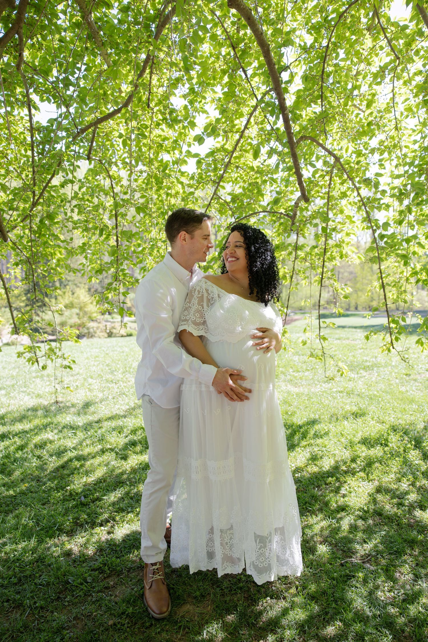Expecting couple embracing under lush DMV trees during maternity session, Rhen Marie Photography capturing authentic moments