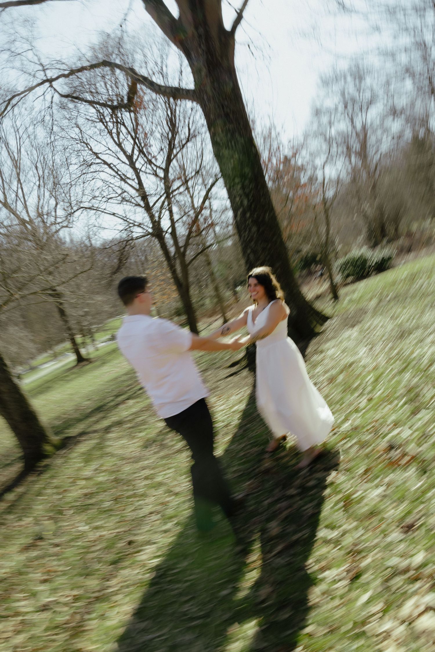 Couple holding hands and spinning in a sunlit DMV park during an outdoor engagement session, captured by Rhen Marie Photography