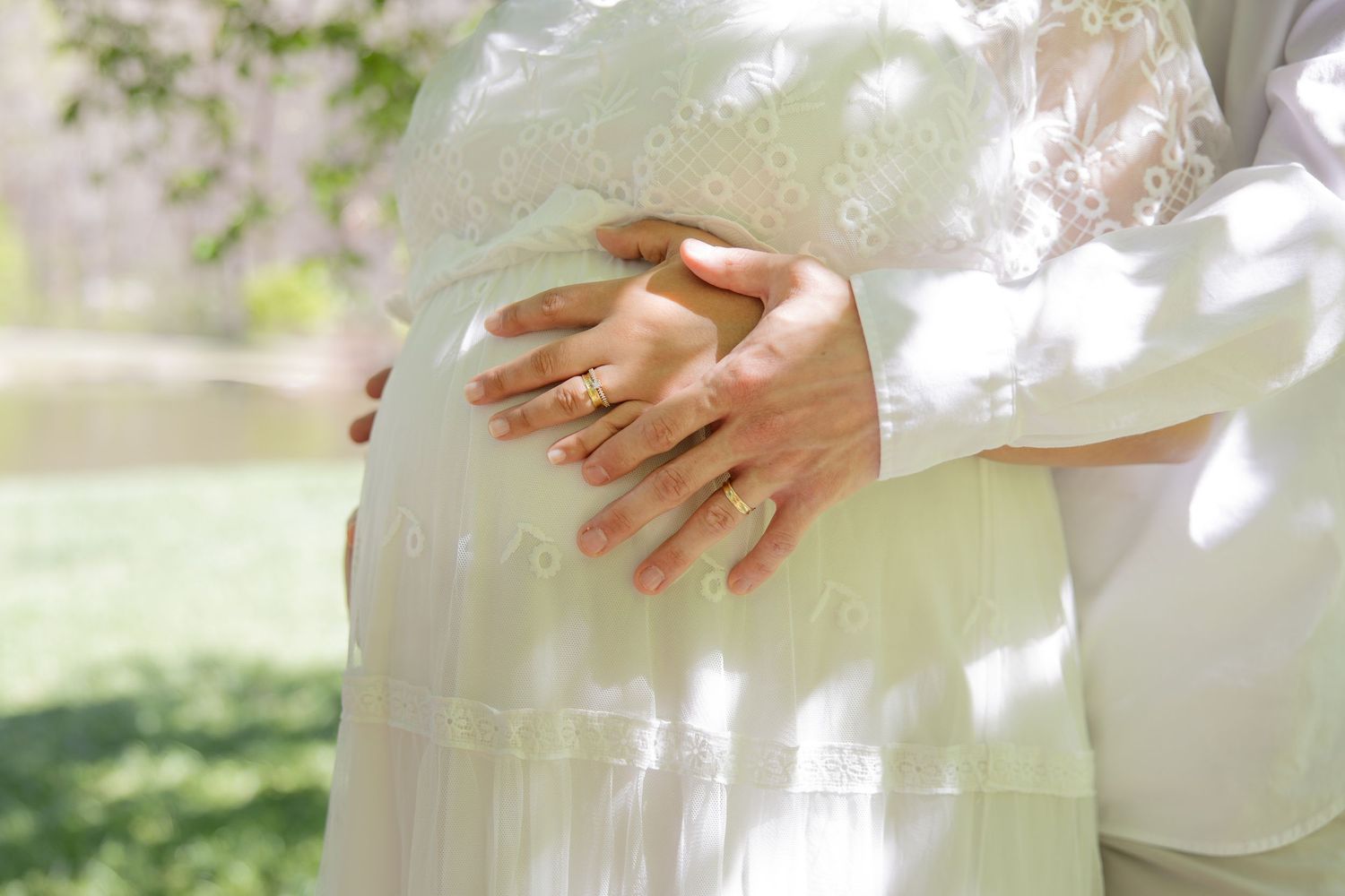 Couple’s hands tenderly on pregnant belly during outdoor maternity session in the DMV, natural sunlight, Rhen Marie Photography