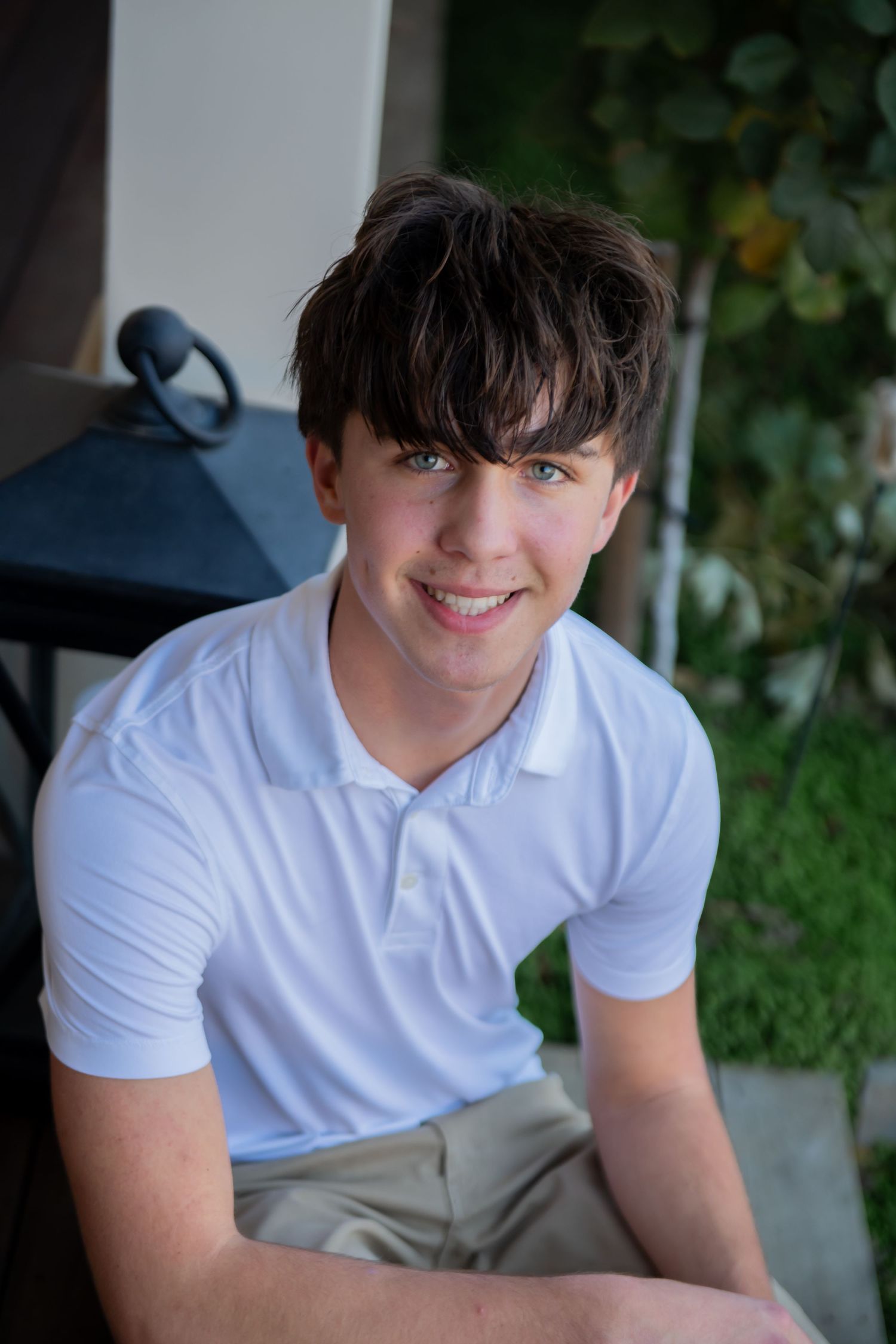 Portrait of smiling young person with dark hair wearing a white polo shirt sitting outdoors.