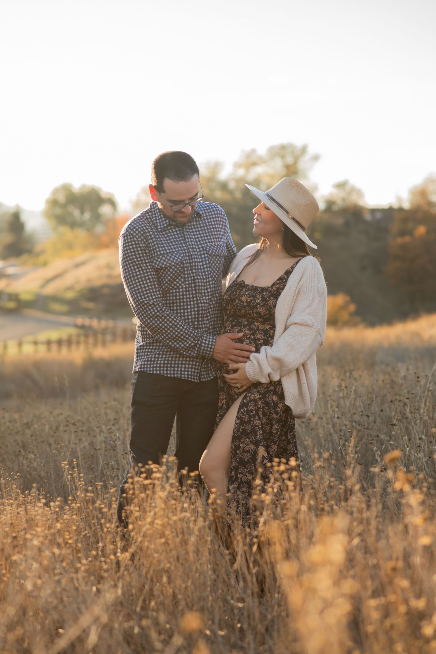 A couple stands together in a golden field at sunset enjoying an intimate moment in nature.
