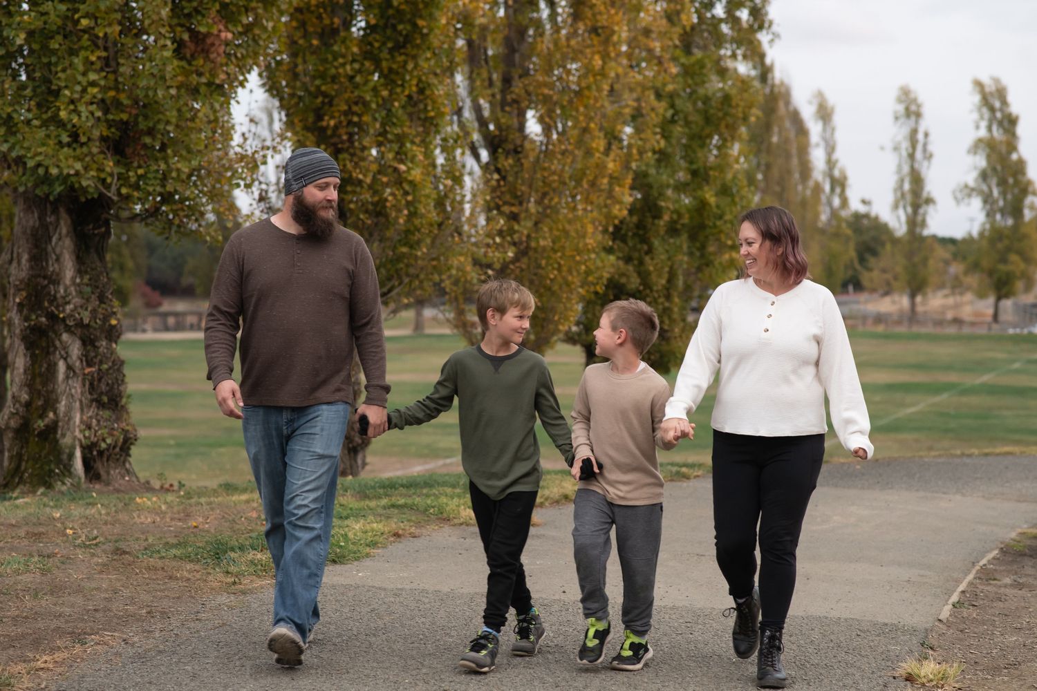 A family of four walking together on a path alongside trees during autumn season.
