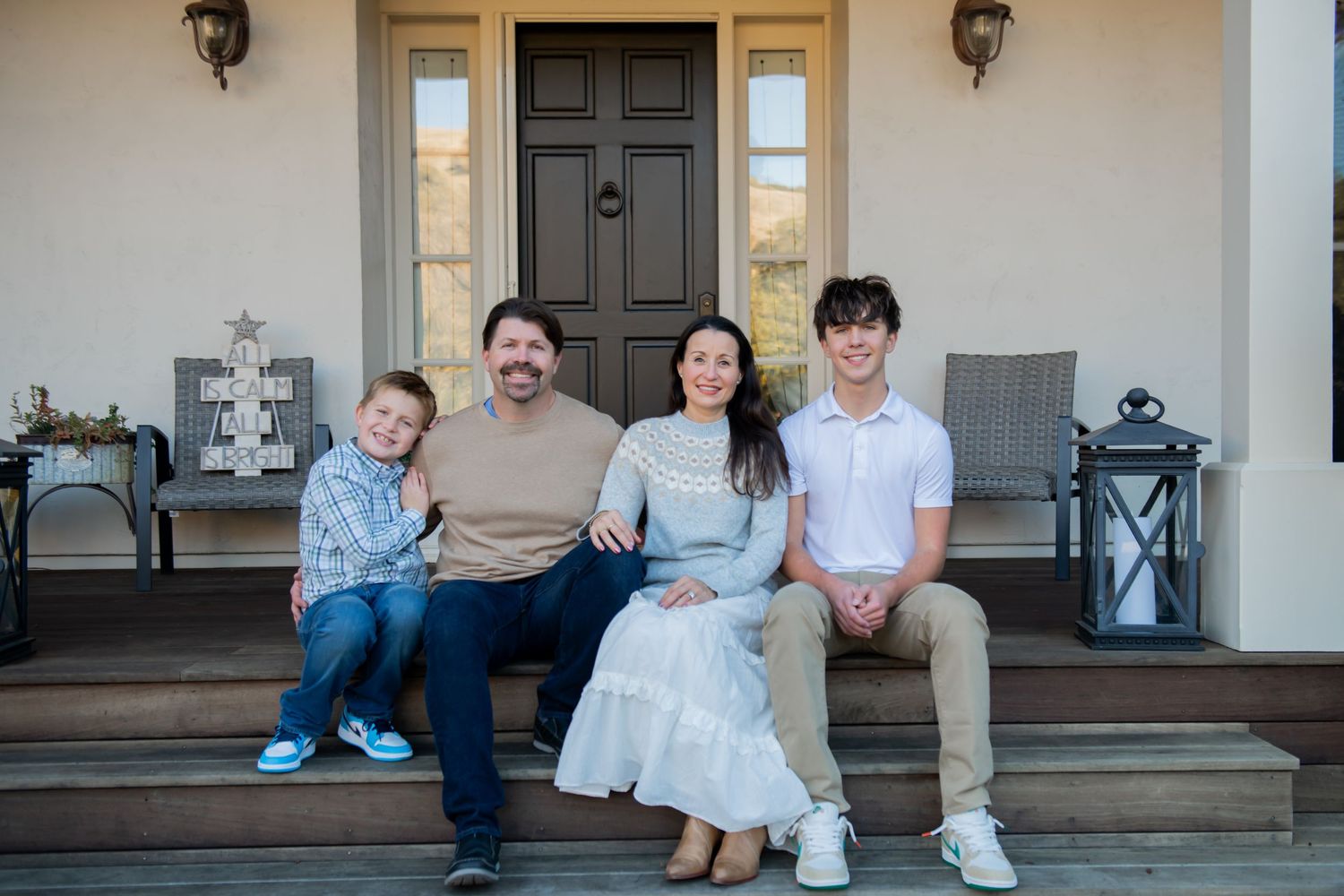 A family sits together on the front steps of their home with decorative lanterns on either side.