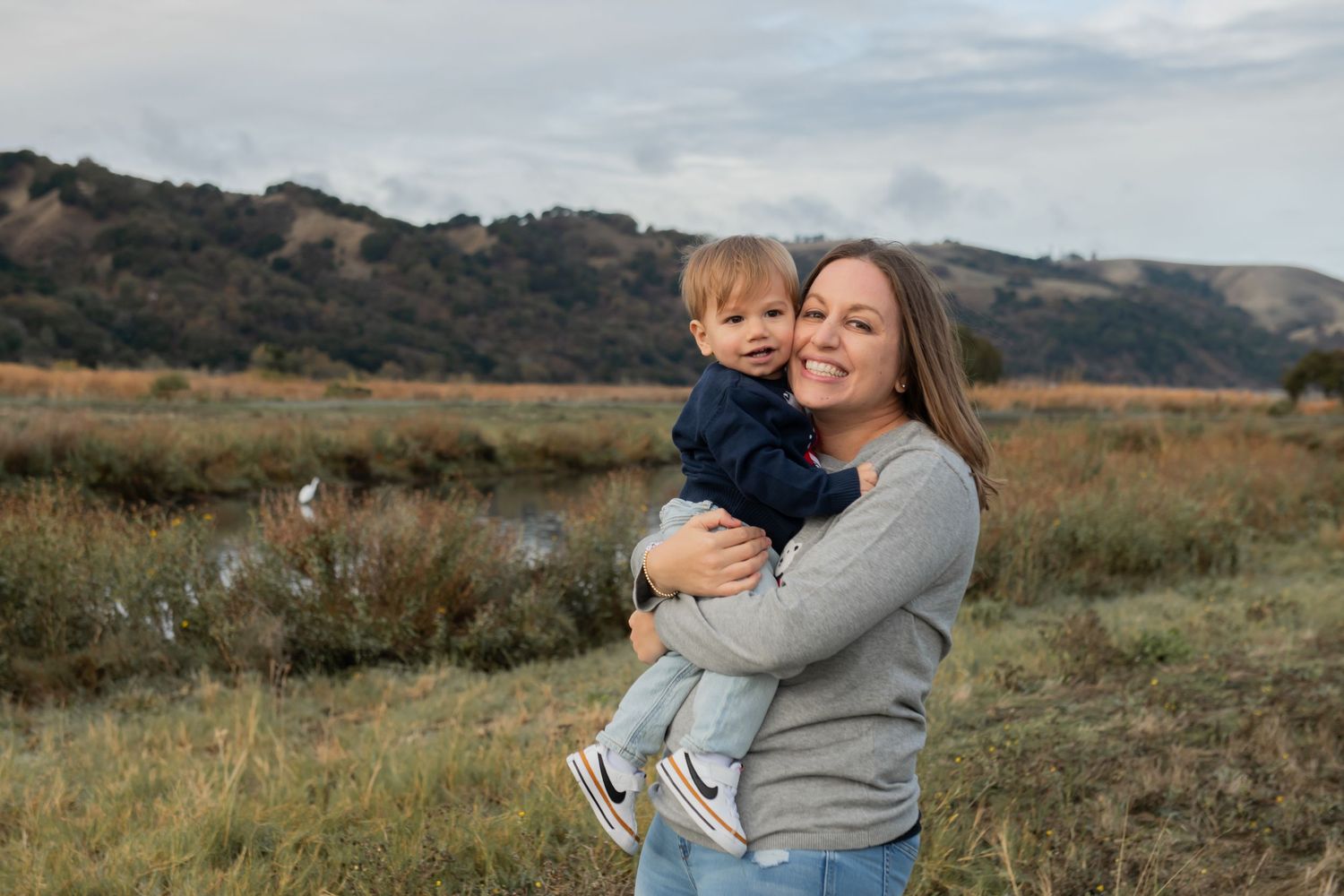 A Mother and child share a joyful moment together in an autumn field with rolling hills in the background.