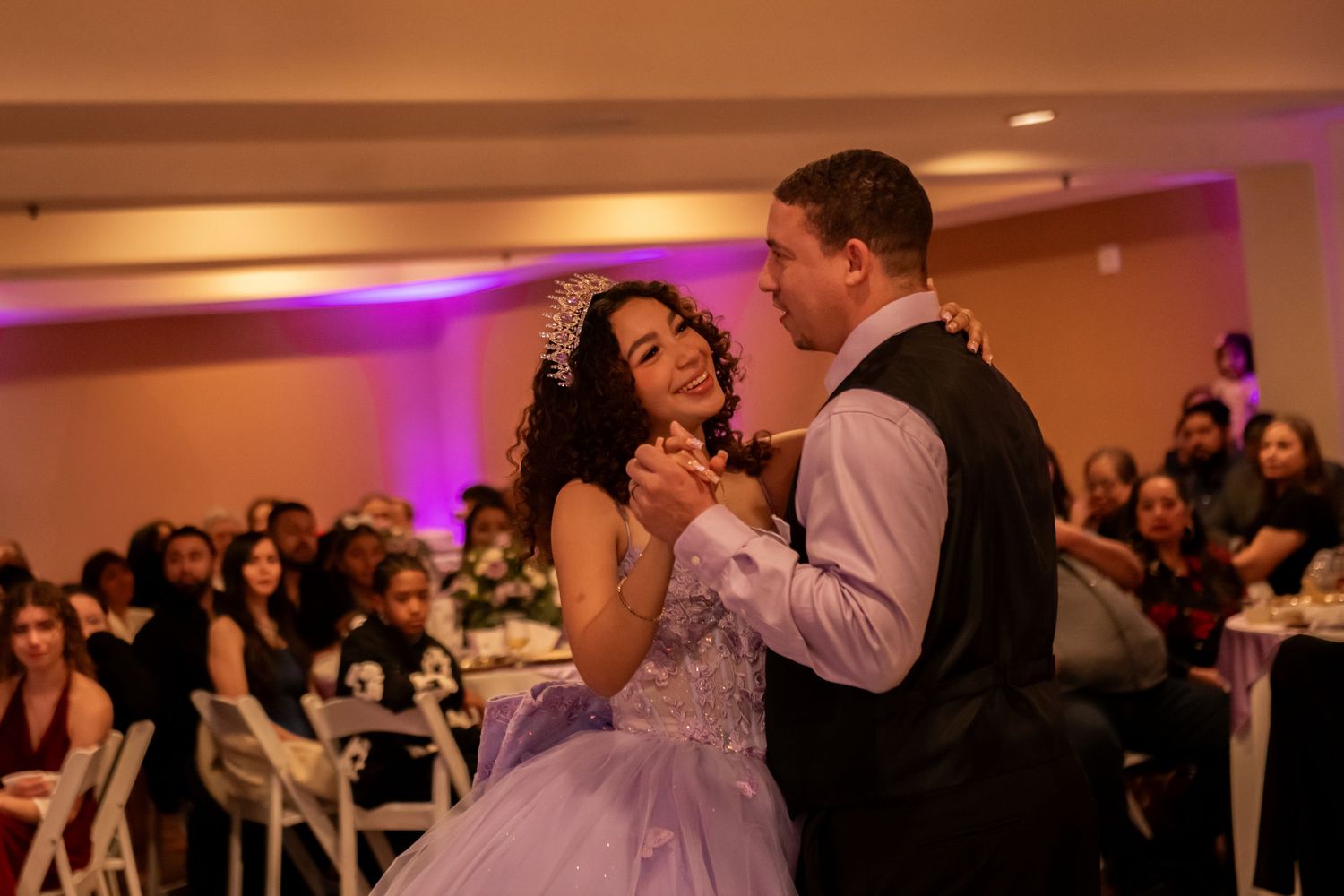 A couple shares a romantic dance together at a wedding reception with purple uplighting in the background.