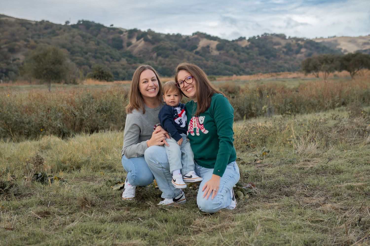 Two people kneeling in a field with rolling hills in the background during golden hour.