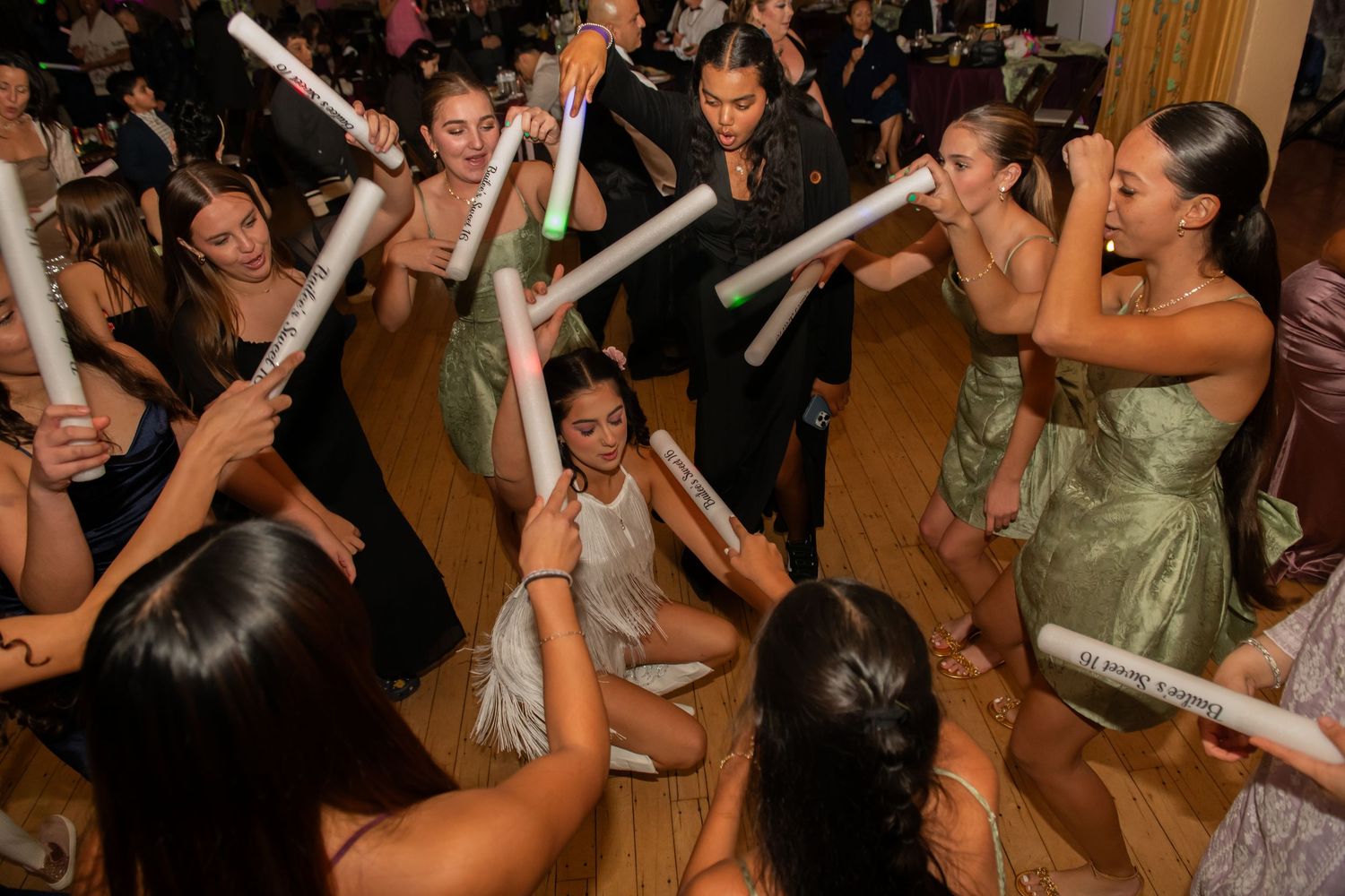 Crowd of party guests dancing and waving glowing light sticks at a celebration event in a ballroom.