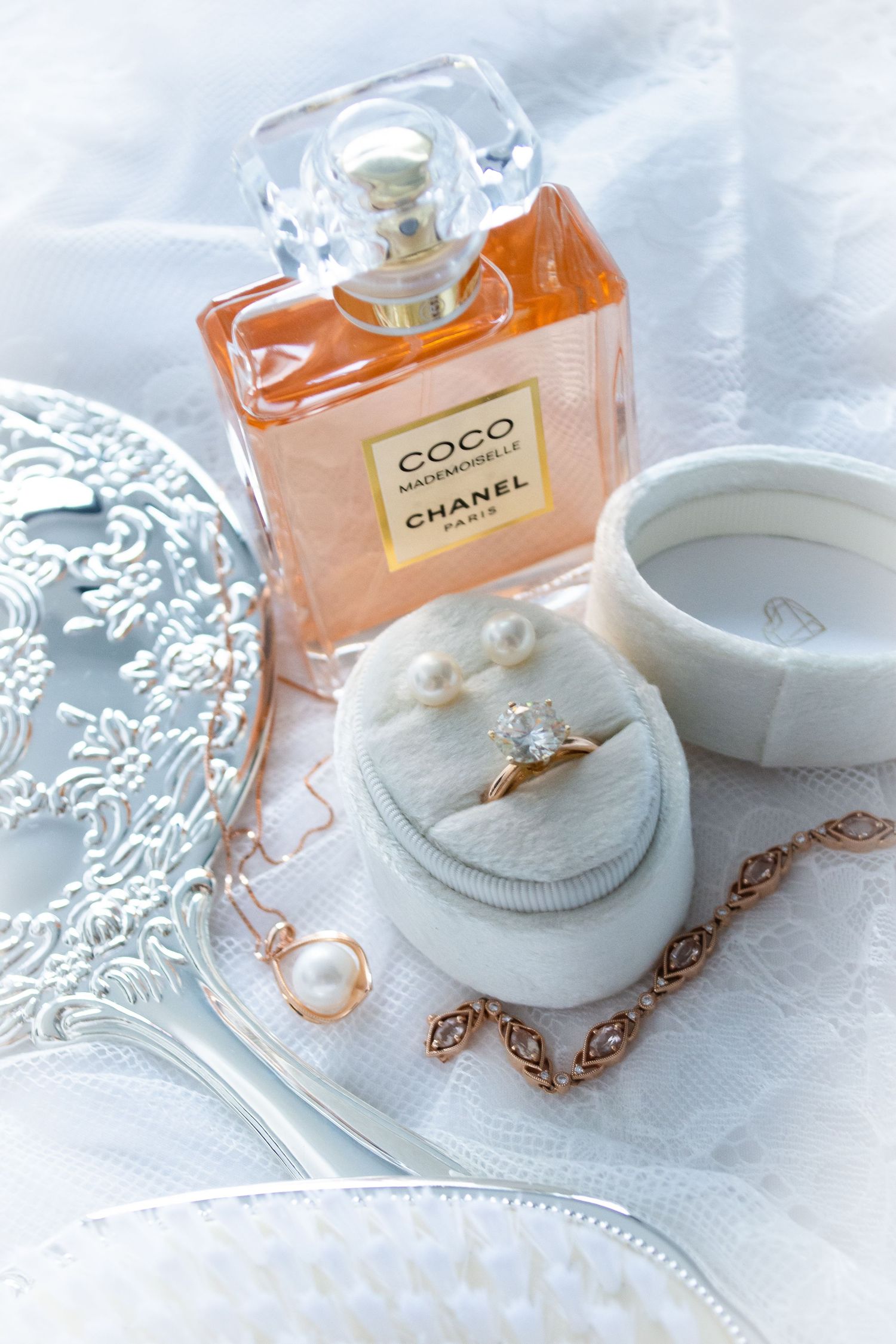 A luxurious Chanel Coco perfume bottle with jewelry box, pearl necklace, and ring on delicate white lace background.