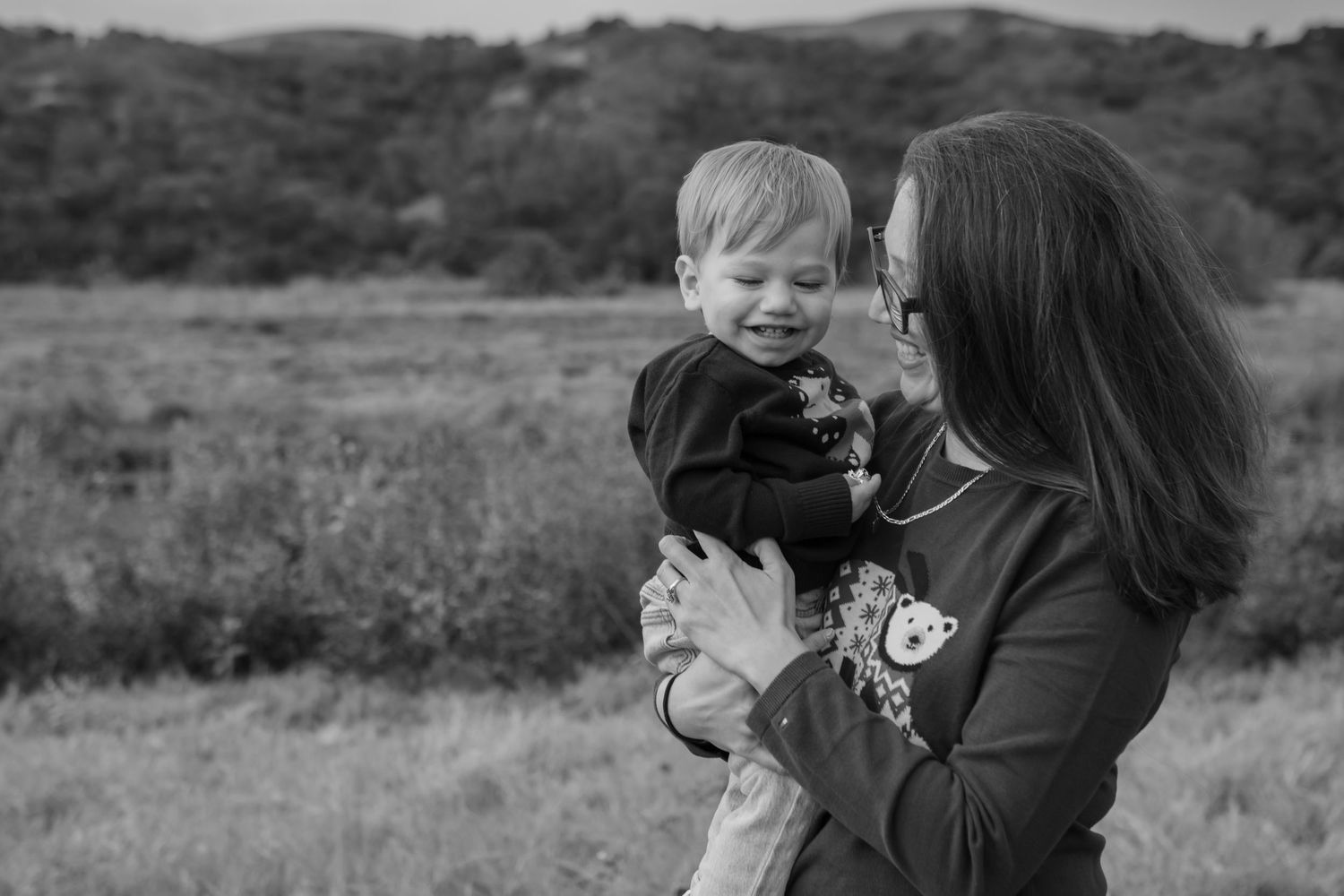 Black and white portrait of a child and adult embracing in a rural field with rolling hills in the background.