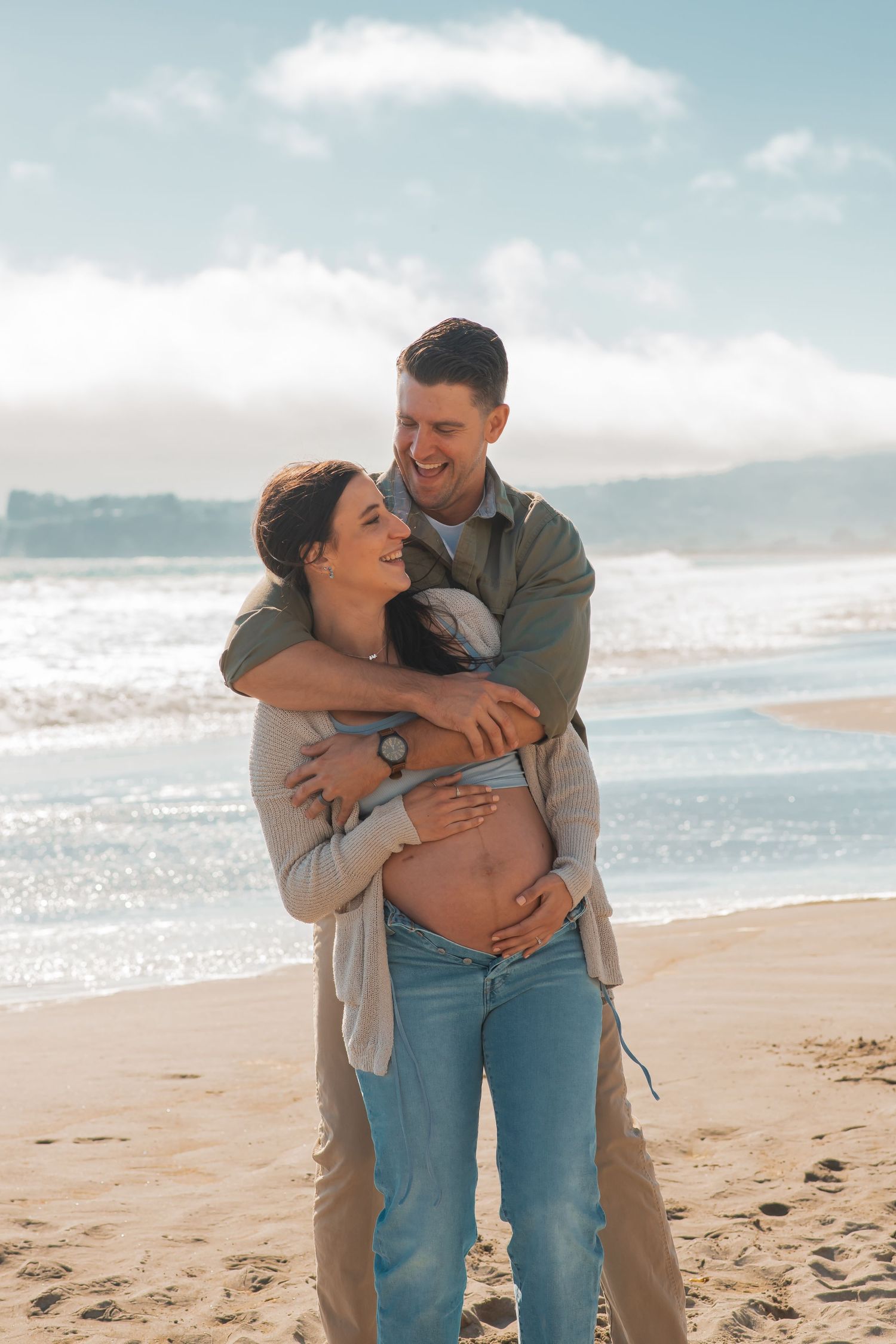 Intimate couple embracing on a sunny beach as they share a tender moment together during a maternity photoshoot.