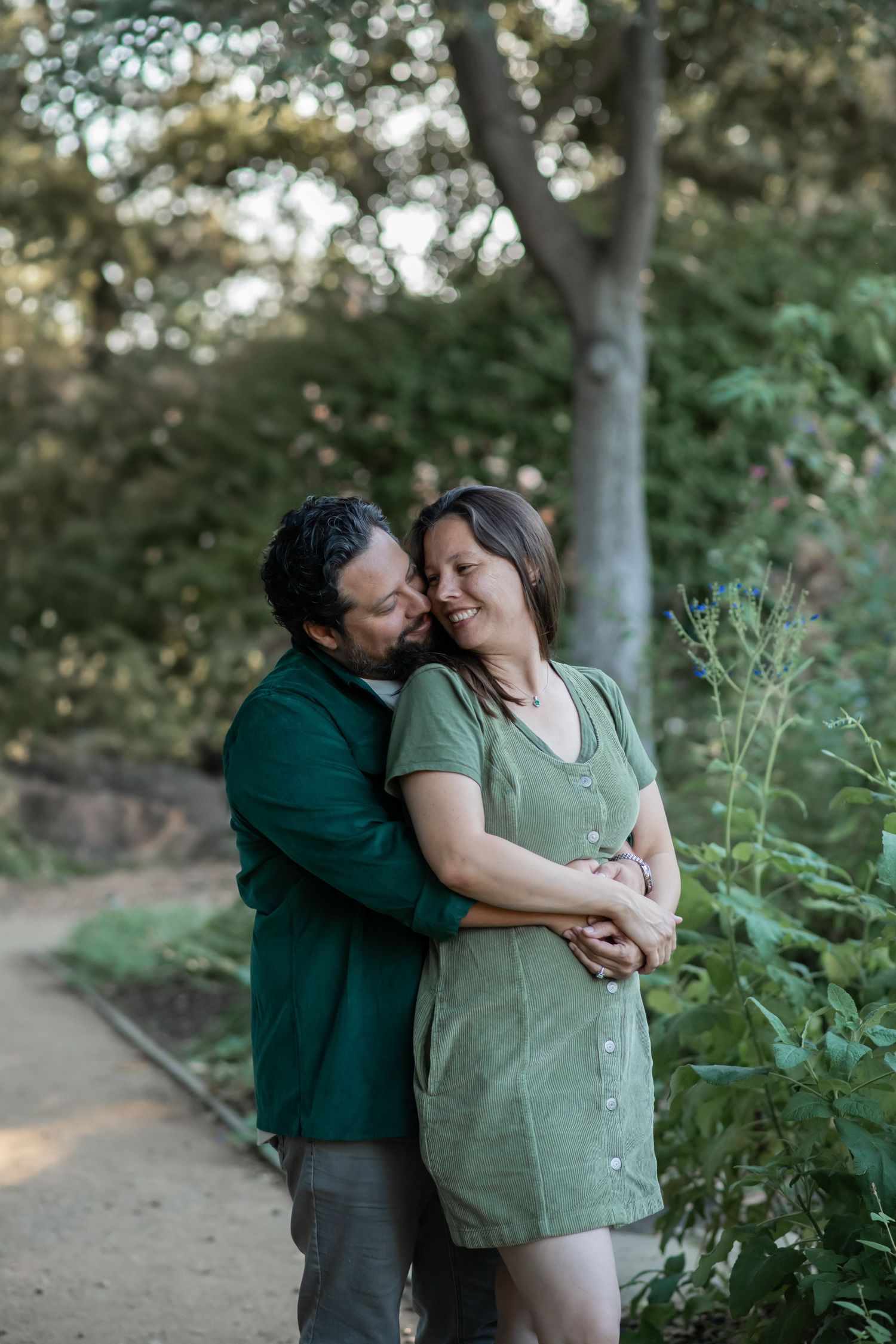 A couple embraces tenderly on a tree-lined dirt path during a romantic outdoor photo session.