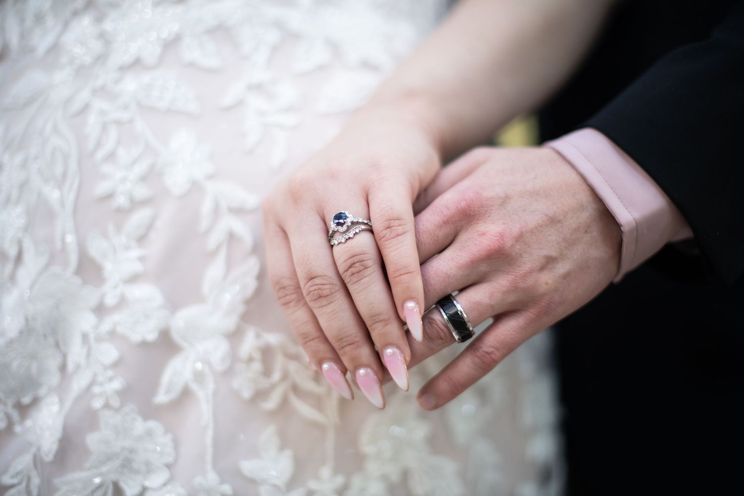 Close up of newlywed couple's hands showing wedding rings against white lace dress.
