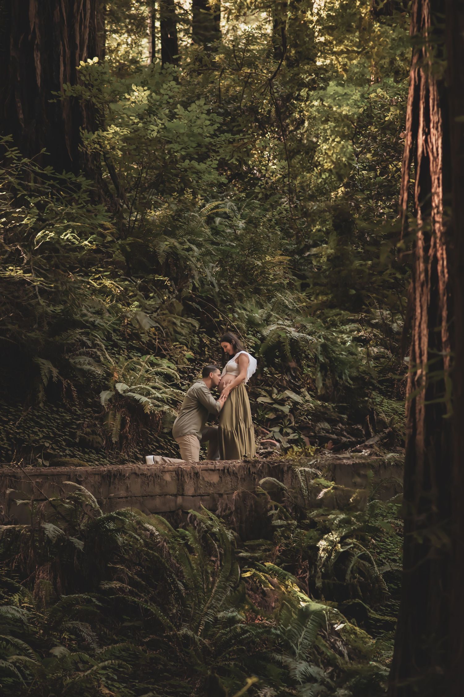 Elegant couple shares intimate moment among towering redwood trees and lush ferns in a magical forest setting.