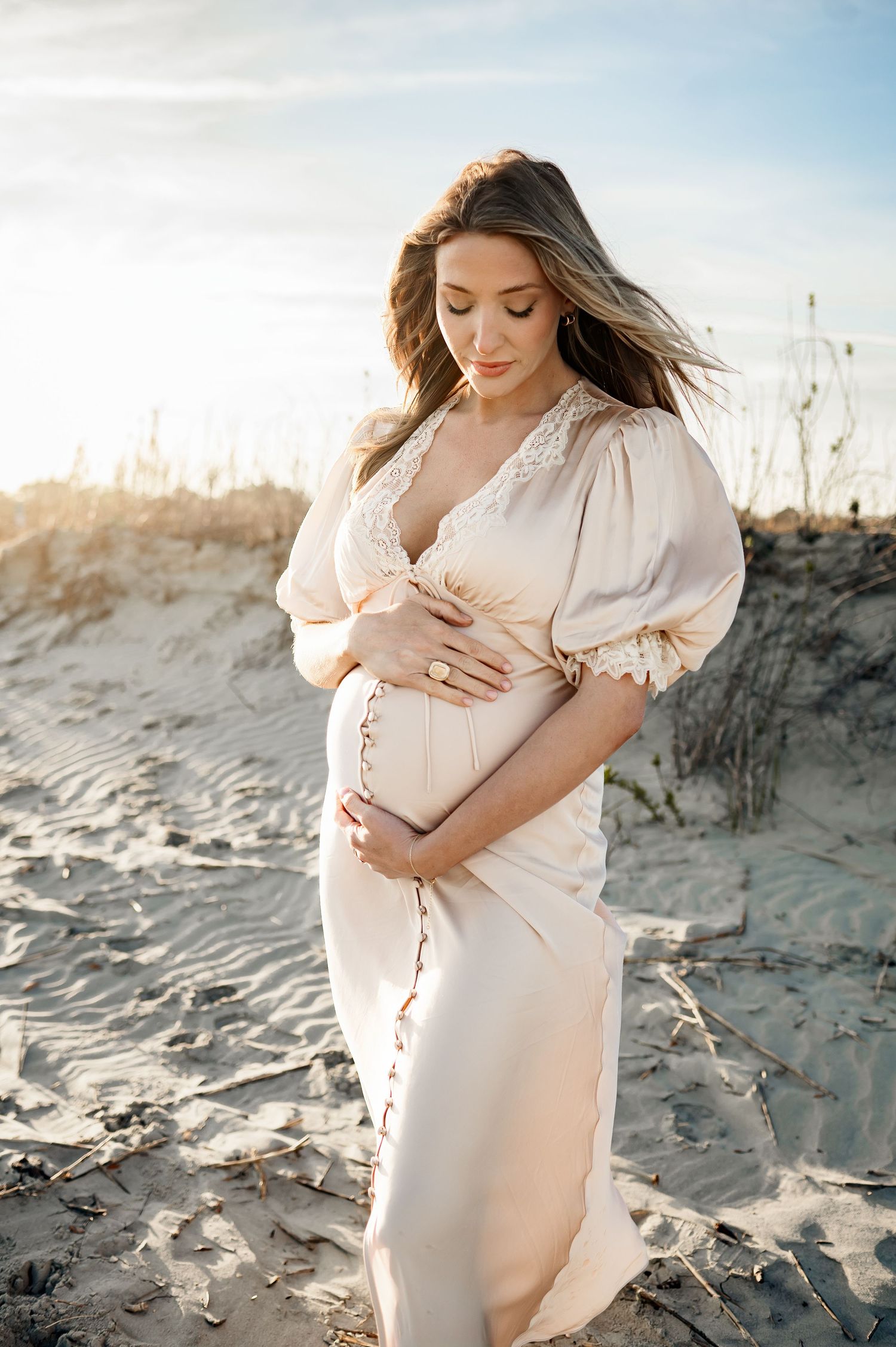Mother looks down at her growing belly during a sunset photography session with a Raleigh maternity photographer