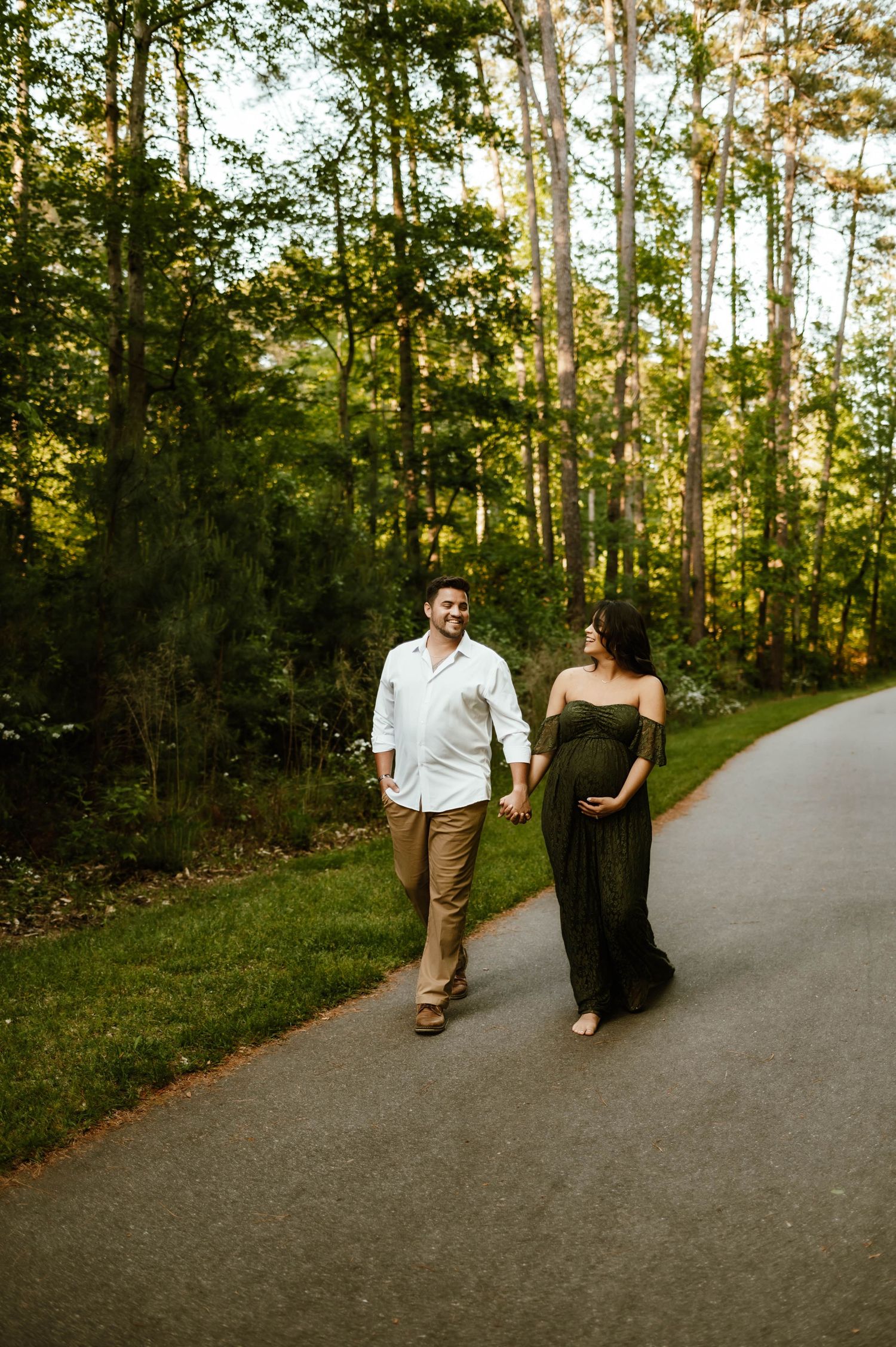 A couple walks together on a winding path through sun-dappled woods during a warm afternoon with affordable photograher raleigh