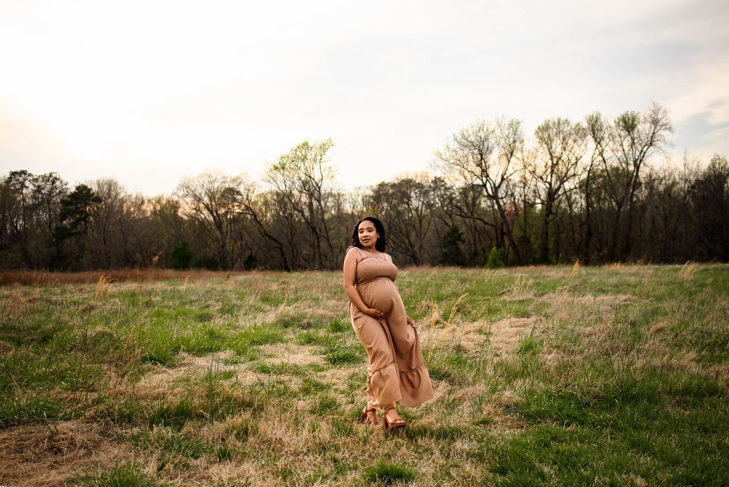 A maternity photo in a flowing peach dress captured during golden hour in a serene field with wake forest maternity photographer