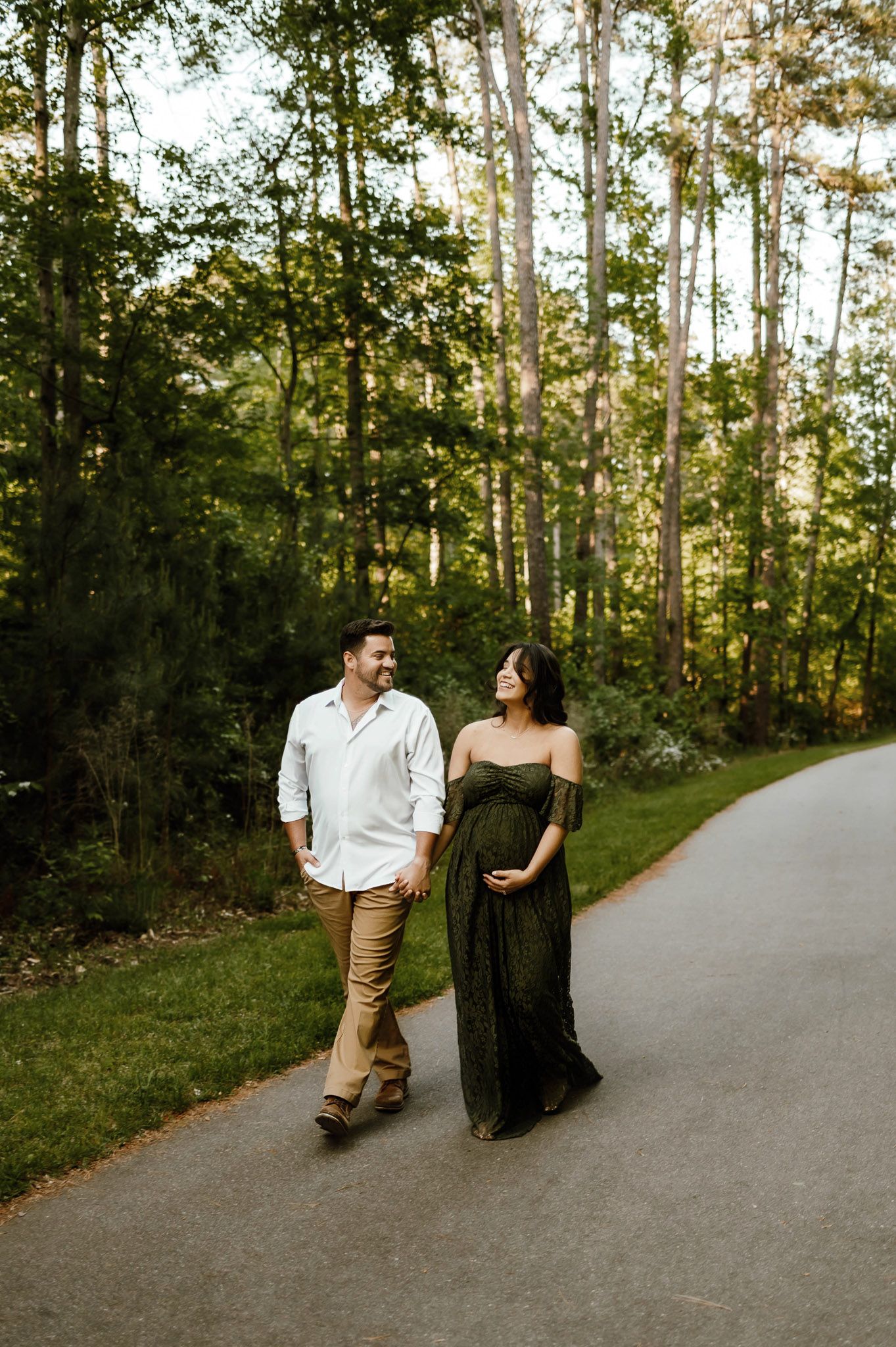 Expectant couple walking hand in hand along a forest path during an outdoor maternity photography session in Raleigh NC