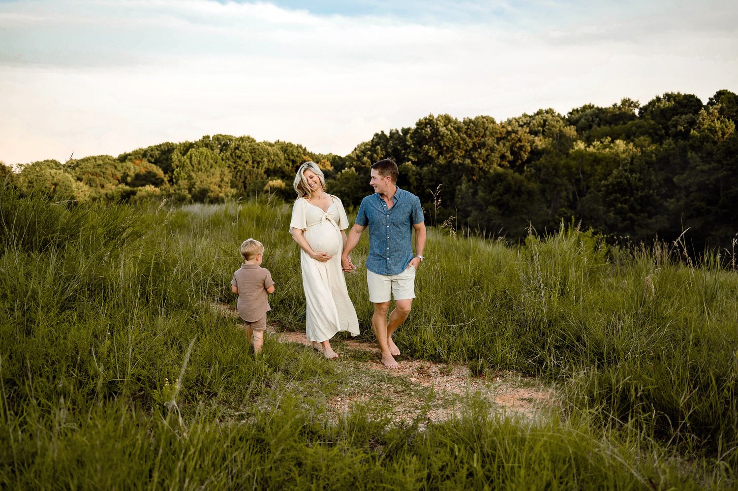 Expecting parents walking through a grassy field with their toddler during a maternity photography session near Raleigh NC