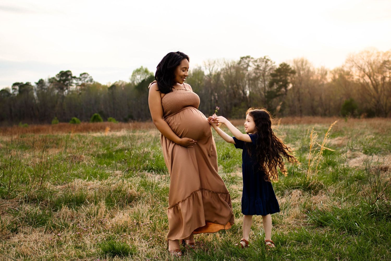 A touching outdoor maternity scene at sunset with a mother and child standing in a grassy field with best raleigh maternity photographer