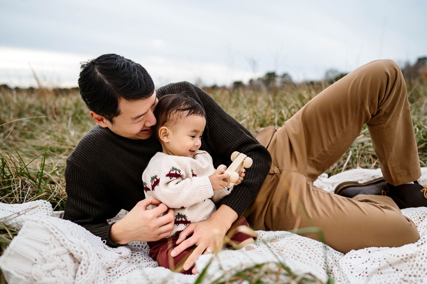 Dad laying on a blanket smiling and playing with his baby during a candid family photo session with Raleigh family photographer