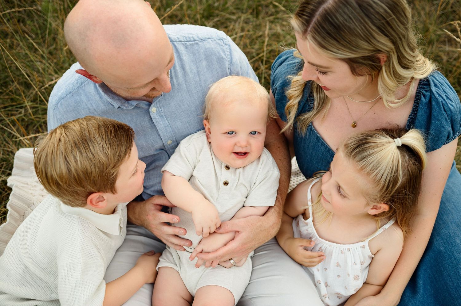 Baby sitting on a parent's lap surrounded by parents and older siblings during an outdoor Raleigh family photography session