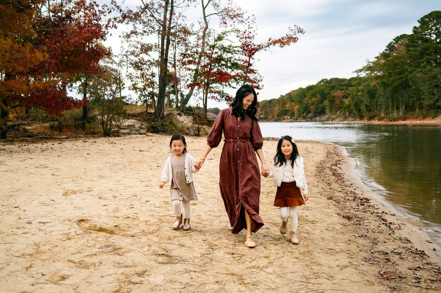 Mother holding hands with her daughters while walking along the lake during a candid family photography session