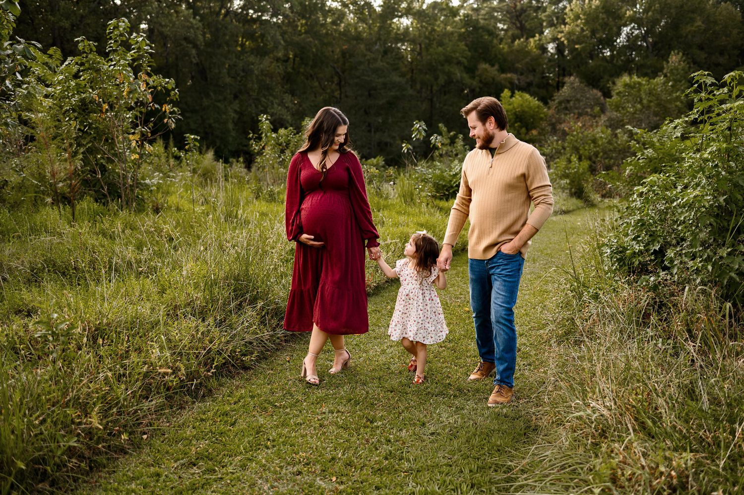 Family maternity photography session outdoors with parents and toddler walking together in Durham NC