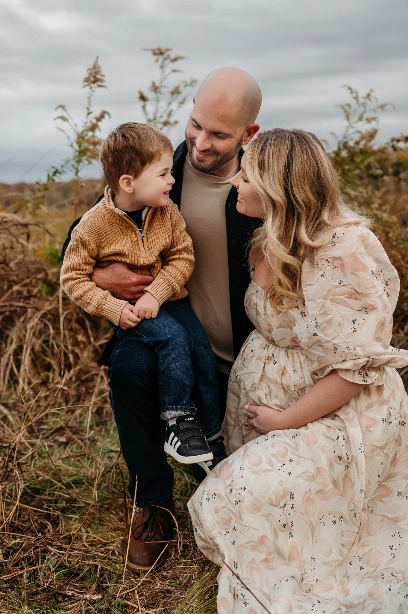 Outdoor maternity photography session with parents and young son sharing a moment together in Apex NC
