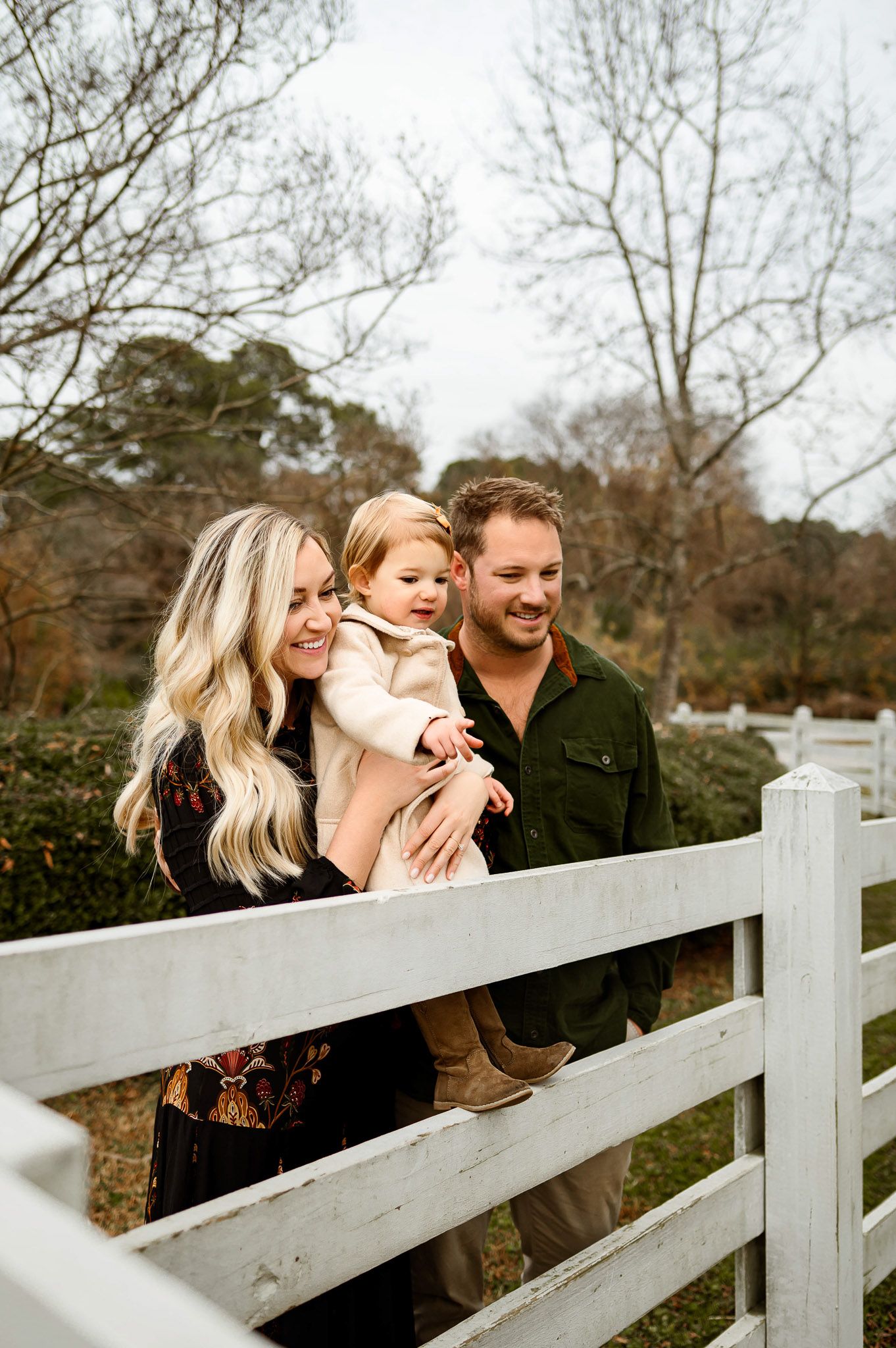 Parents holding their daughter near a white fence during a relaxed outdoor family photography session in Raleigh