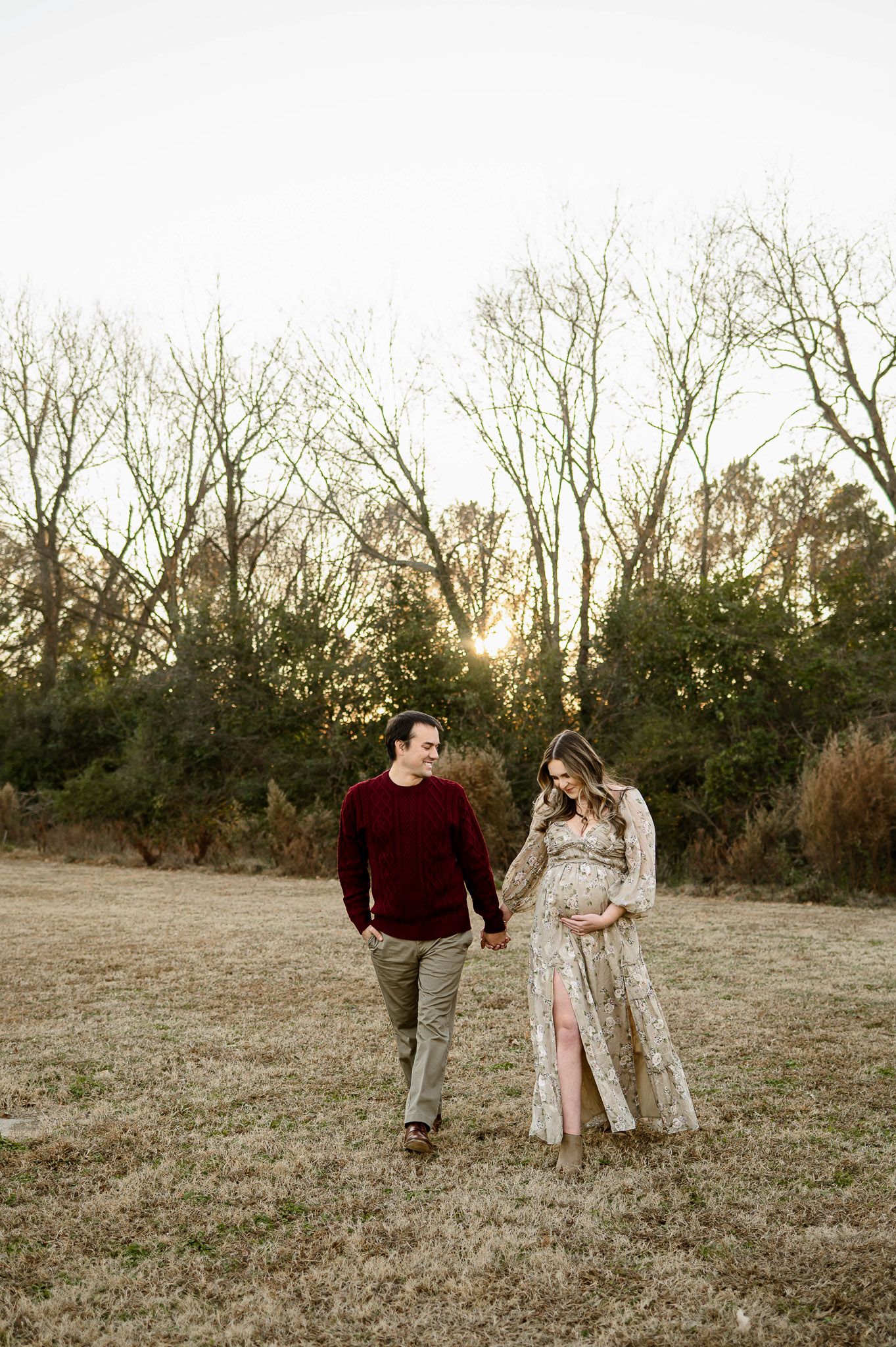 Expecting couple holding hands and walking through a field during a Raleigh maternity photography session