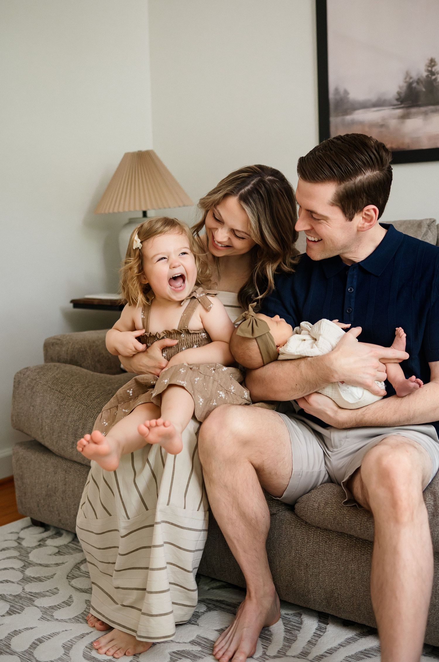 Older sibling laughs while sitting on mother's lap in photo captured by a Raleigh newborn photographer