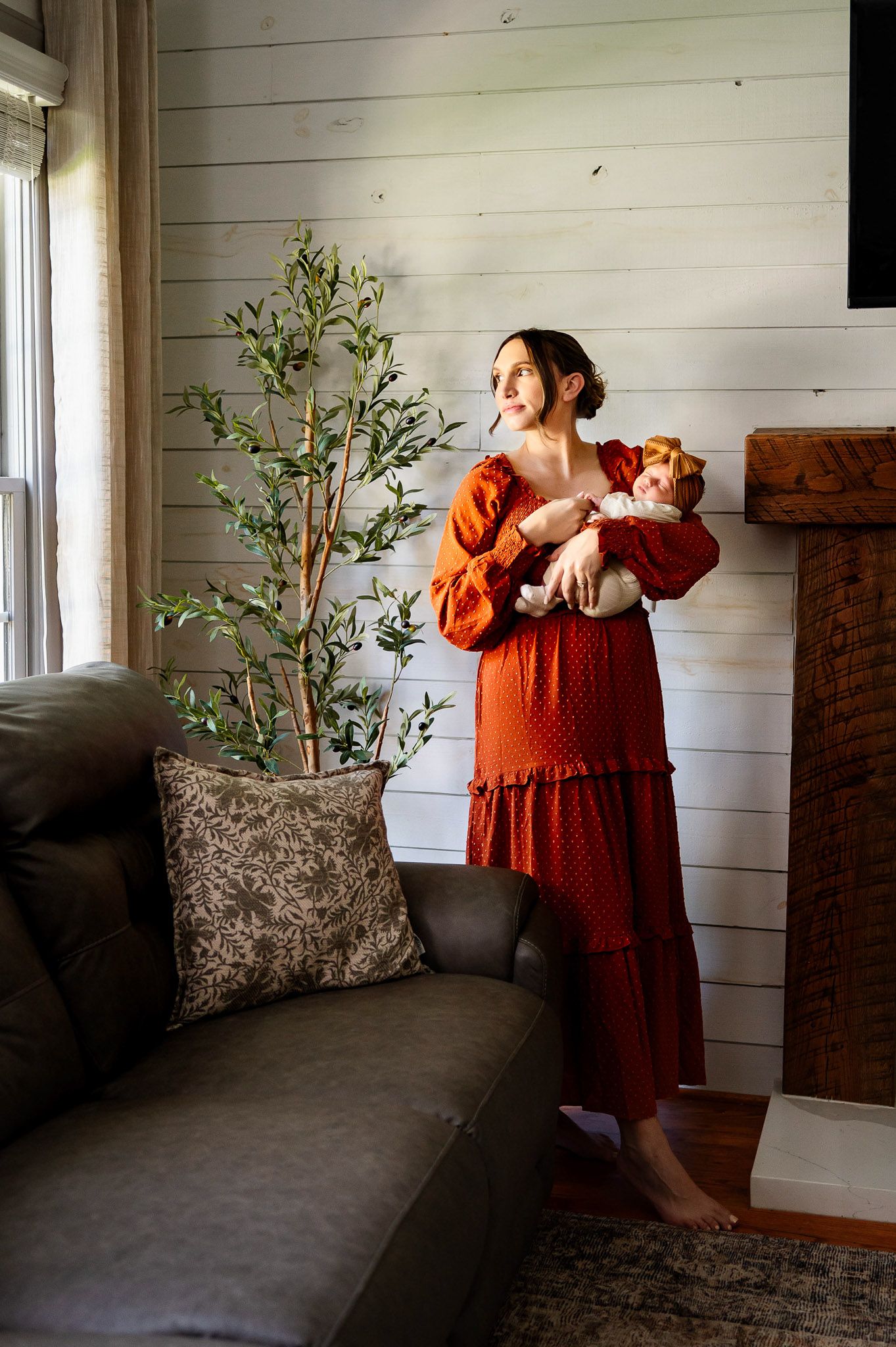 Mother holding her newborn baby near a window during a relaxed in-home newborn photography session in Raleigh North Carolina