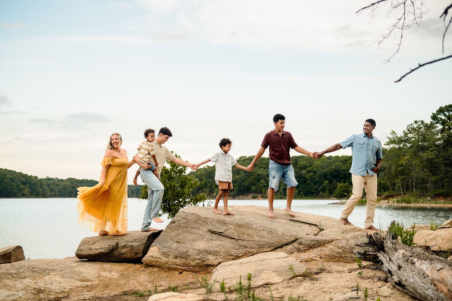 Family of six holding hands on rocks beside a lake during an outdoor Raleigh family photography session