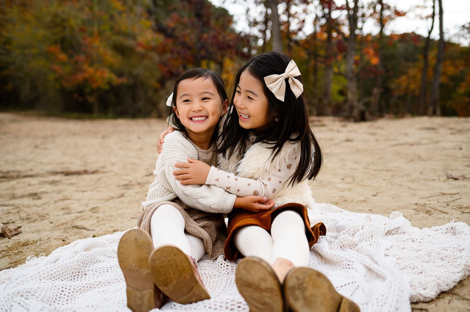 Two sisters hugging while sitting on a blanket during a fall family photography session outdoors in Durham NC