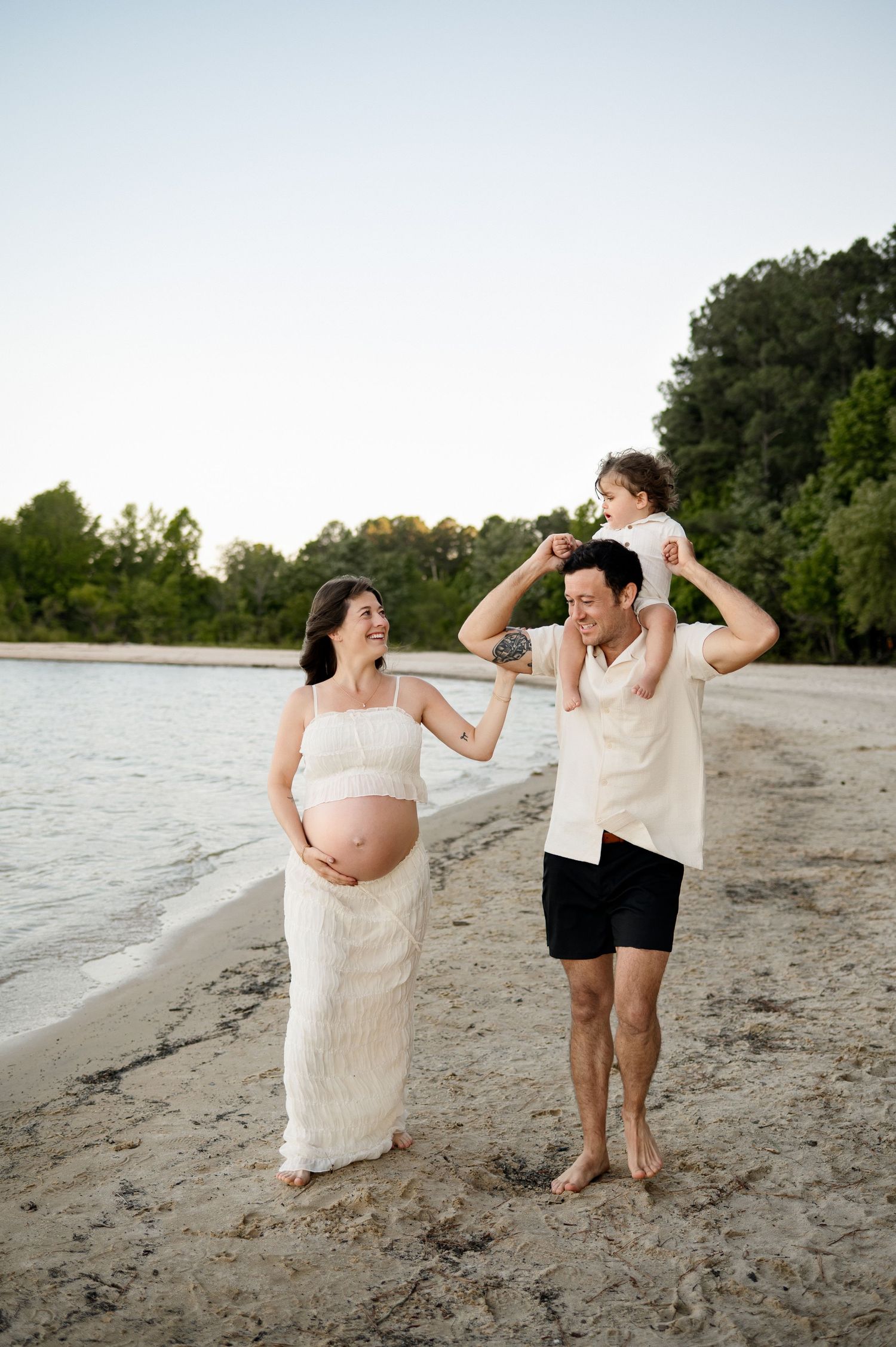 Toddler sits on father's shoulders as family walks together on a beach during a photoshoot with a Cary NC maternity photographer