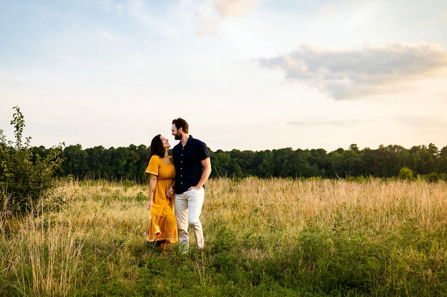 Golden hour couple walking through grassy field during outdoor session photographed by Durham family photographer