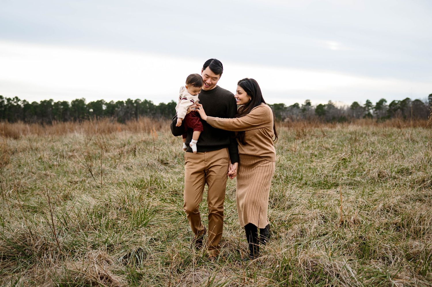 Parents walking together with their baby in an open field during a natural light family session