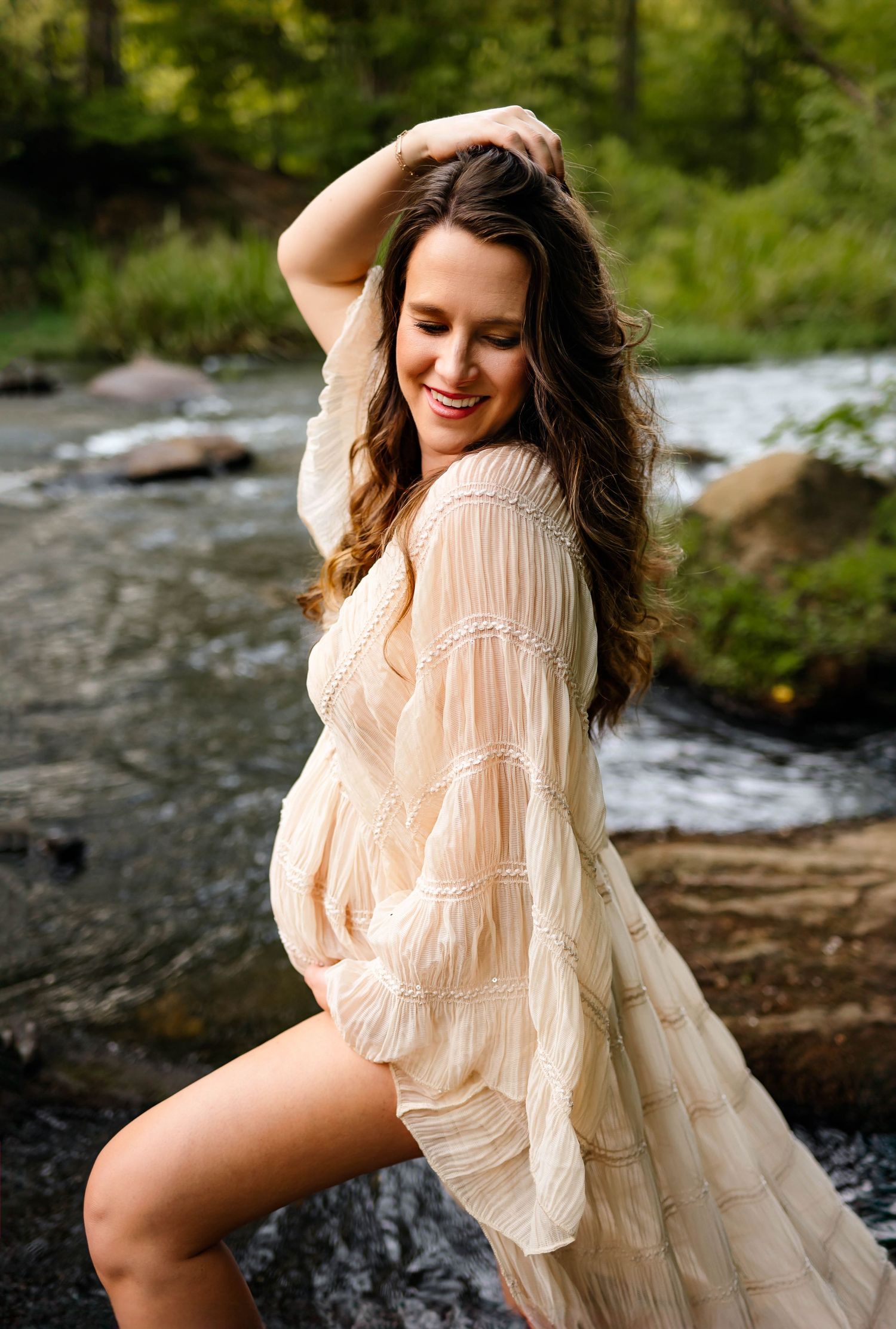 A maternity photograph with mother in a flowing dress posing near a rocky stream with durham maternity photographer