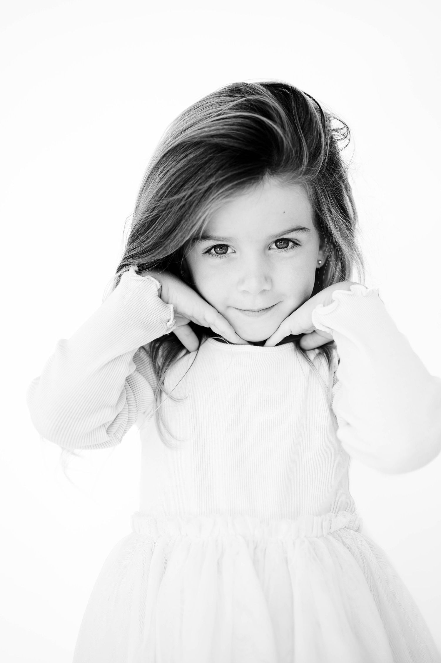 A series of black and white portraits showing a child in white clothing against a bright background during childhood personality photoshoot