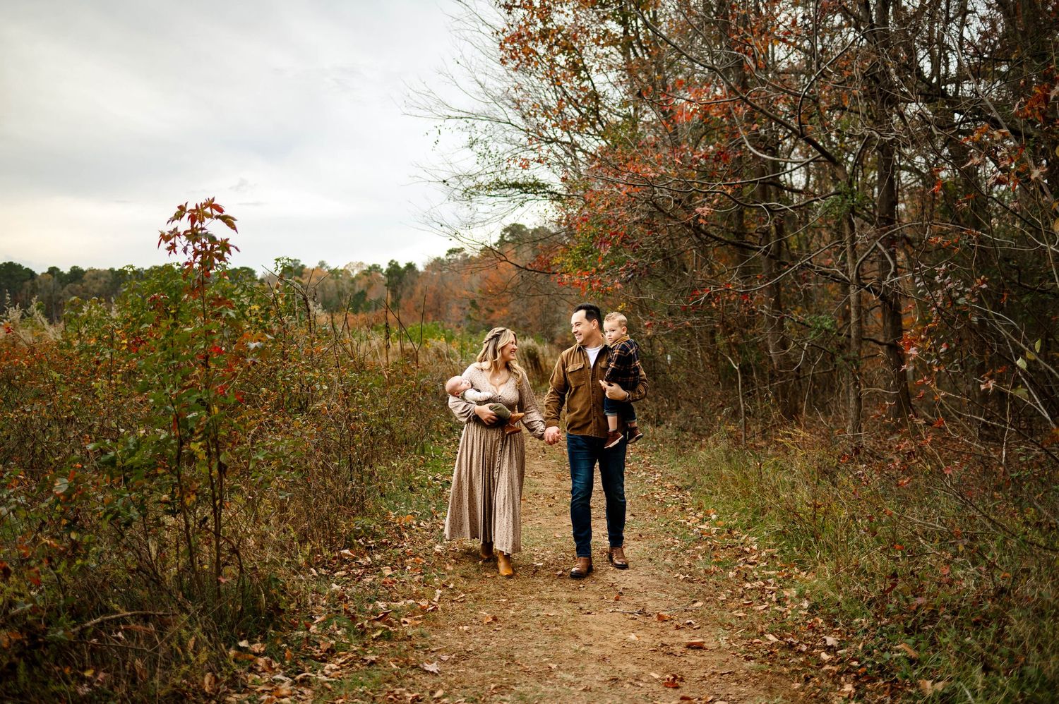 A family walks along a scenic autumn path surrounded by fall foliage and trees in Raleigh NC with family photographer