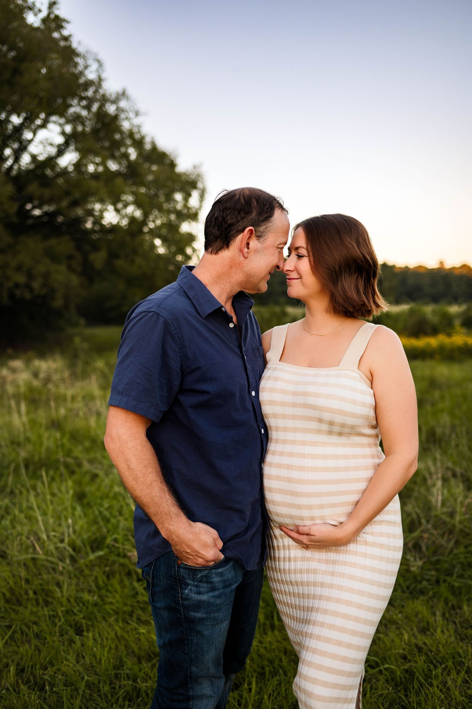 A romantic maternity photo in a field at sunset shows an expecting couple sharing an intimate moment with afforable maternity photographer